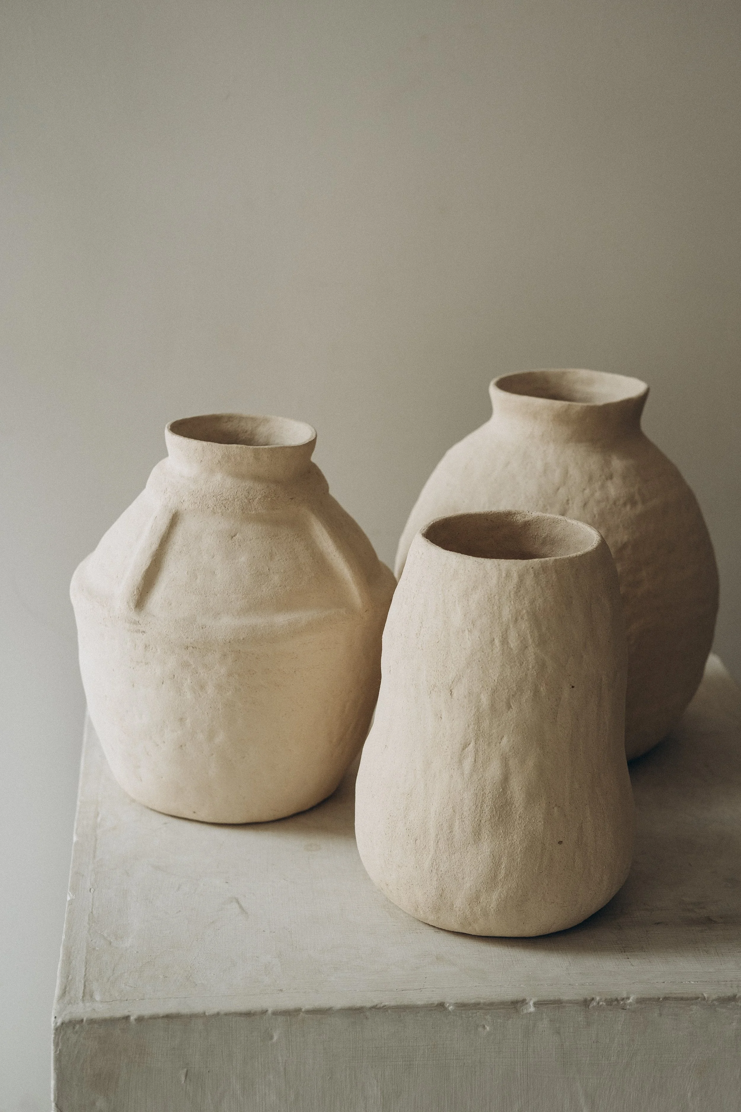 Quatre vases en céramique beige sur une surface blanche, avec un fond neutre.