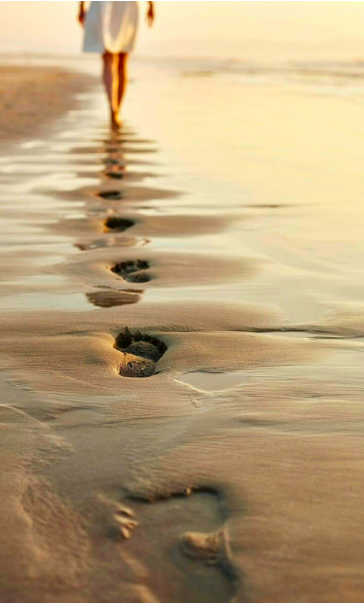 Pas de personne en marche sur la plage avec empreintes dans le sable, soleil couchant à l'horizon.