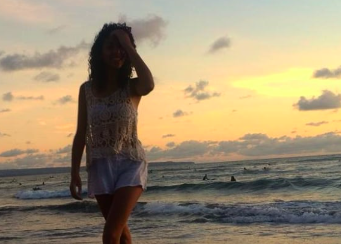 Femme marchant sur la plage au coucher du soleil, portant un haut en crochet et un short en jean, sourire souriant.
