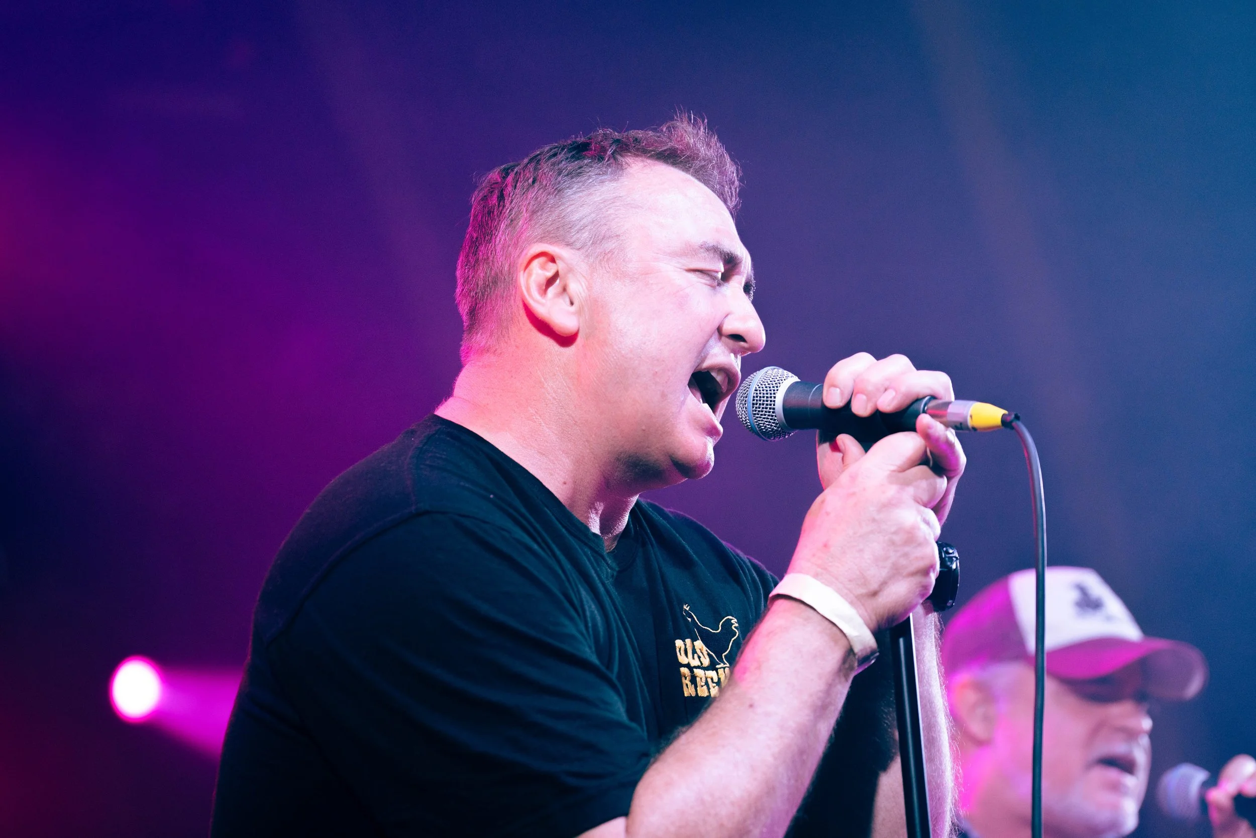 A man passionately singing into a microphone on stage with purple and blue lighting.