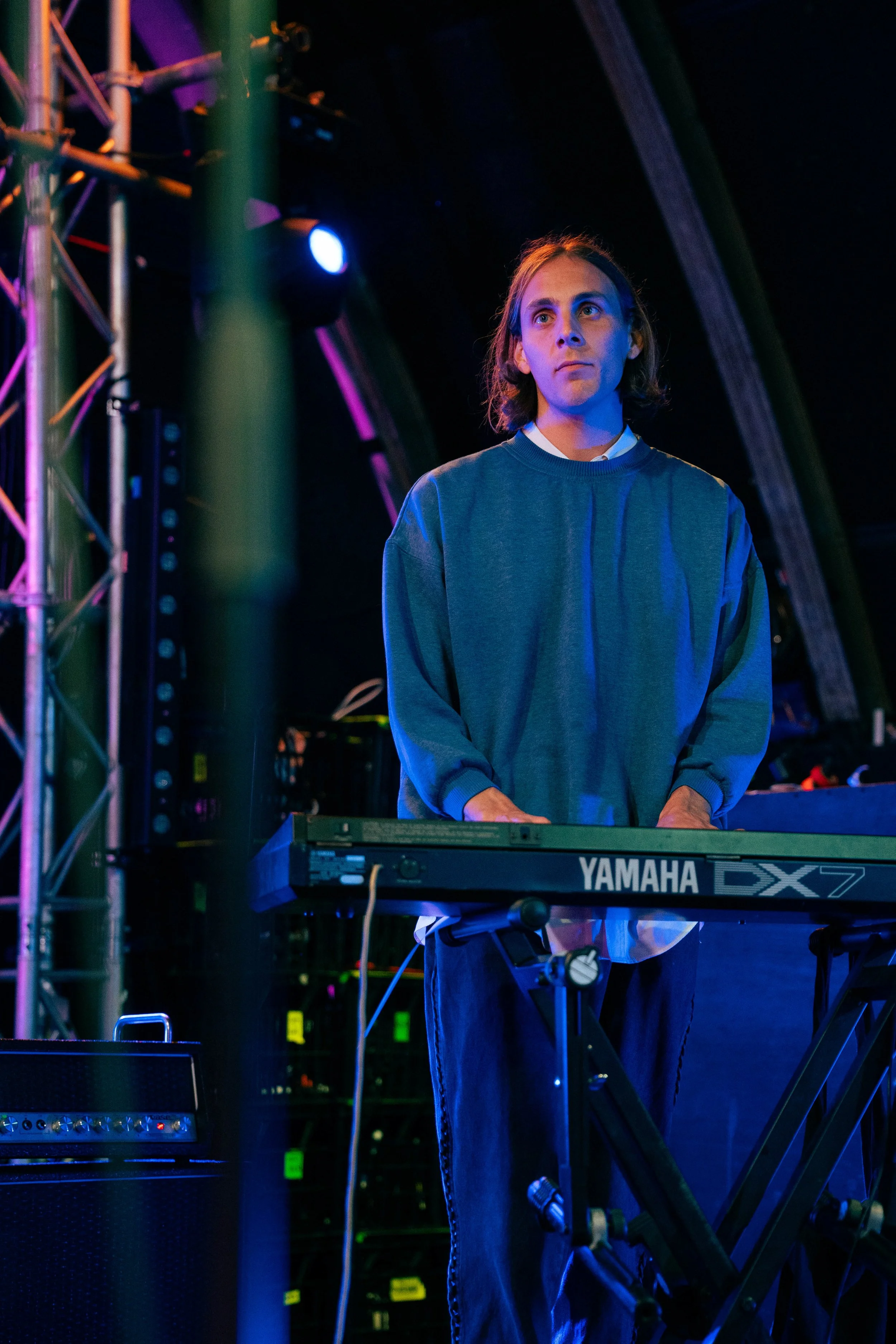 A person standing behind a Yamaha keyboard on stage, surrounded by colorful stage lighting and equipment.