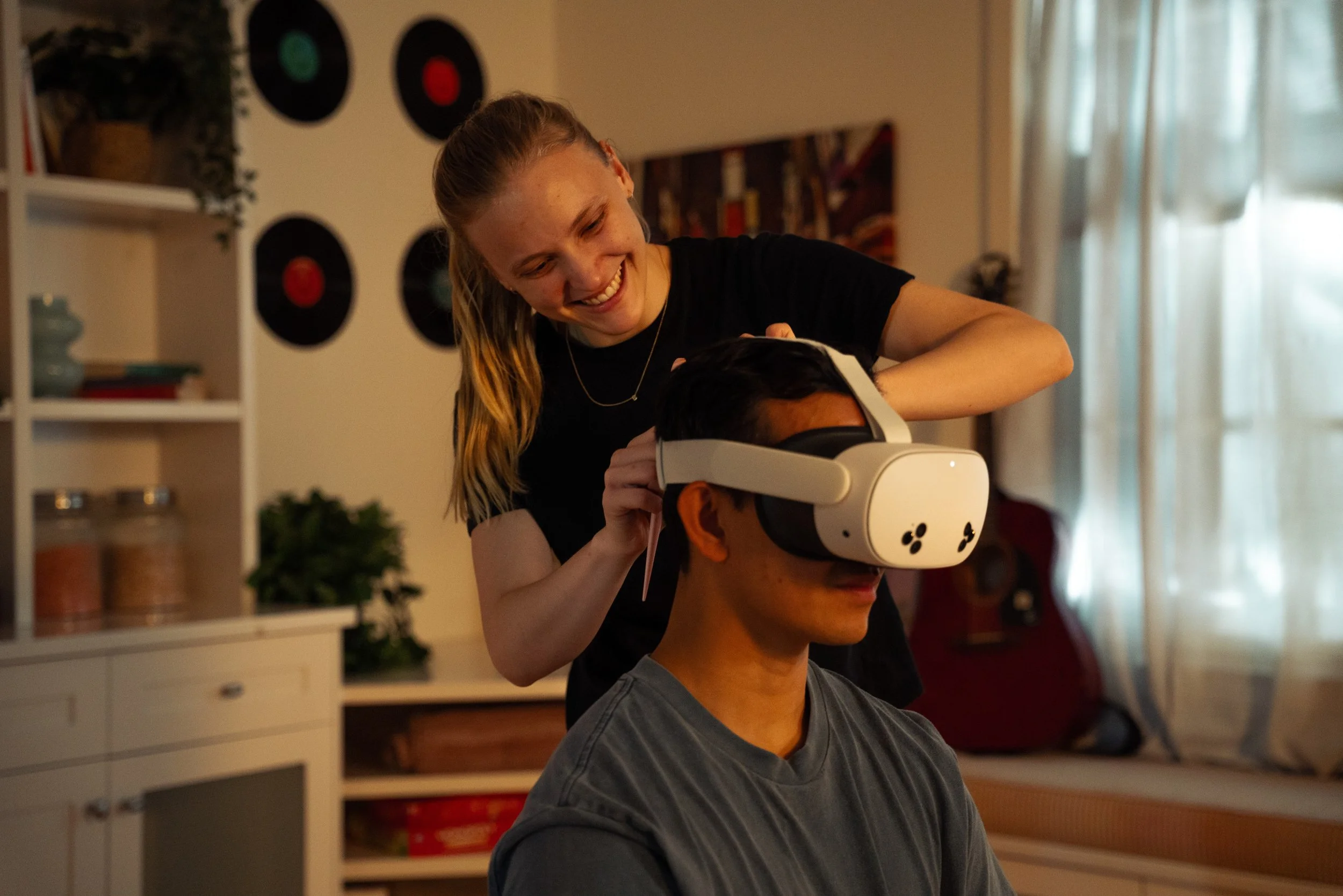 Woman helping a man with a virtual reality headset in a cozy room with curtains.