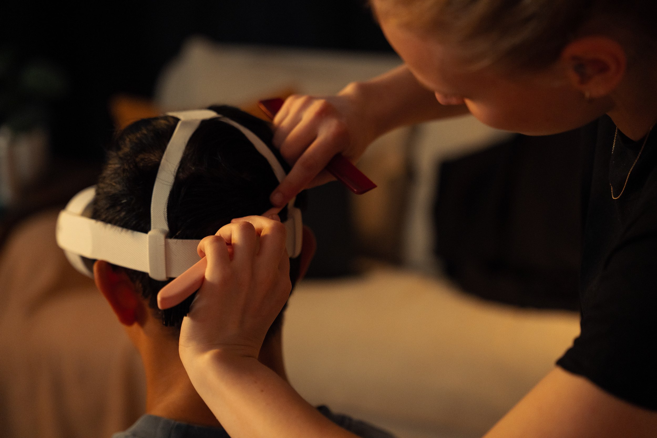 Person holding a child's head steady while applying makeup or face paint, in a dimly lit room.