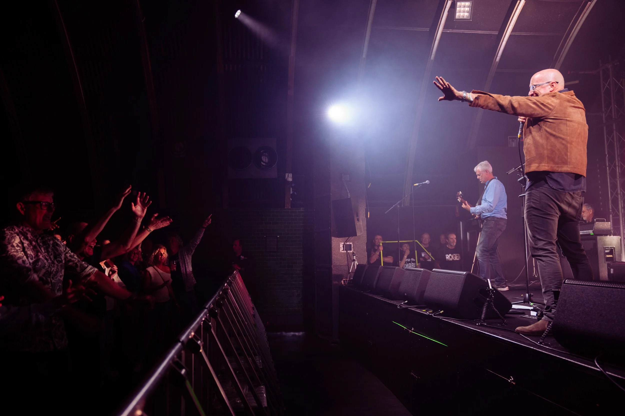 Musicians perform on stage with audience reaching towards them in a concert hall.