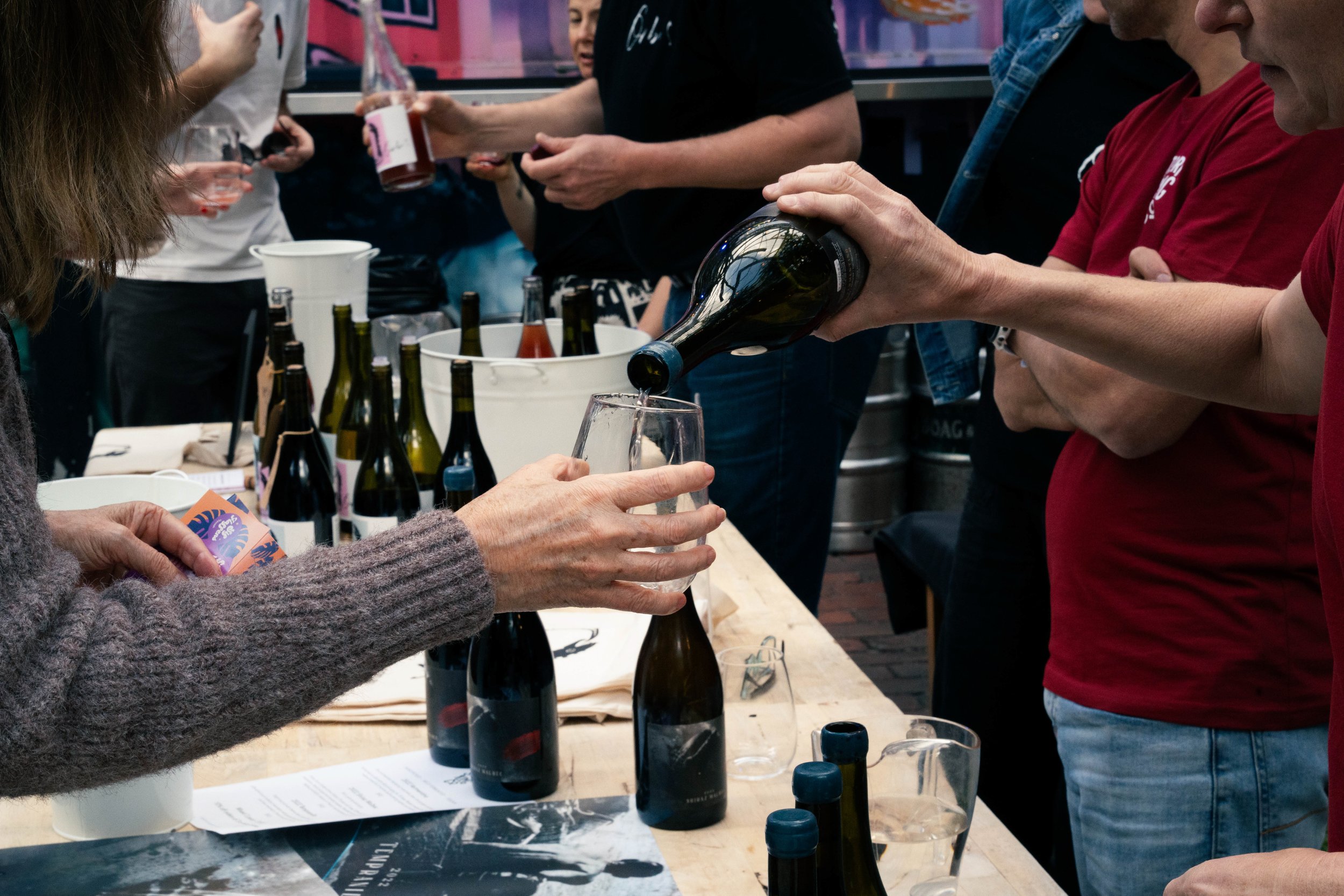 Person pouring wine into a glass at a wine tasting event with bottles and tasting notes on the table.