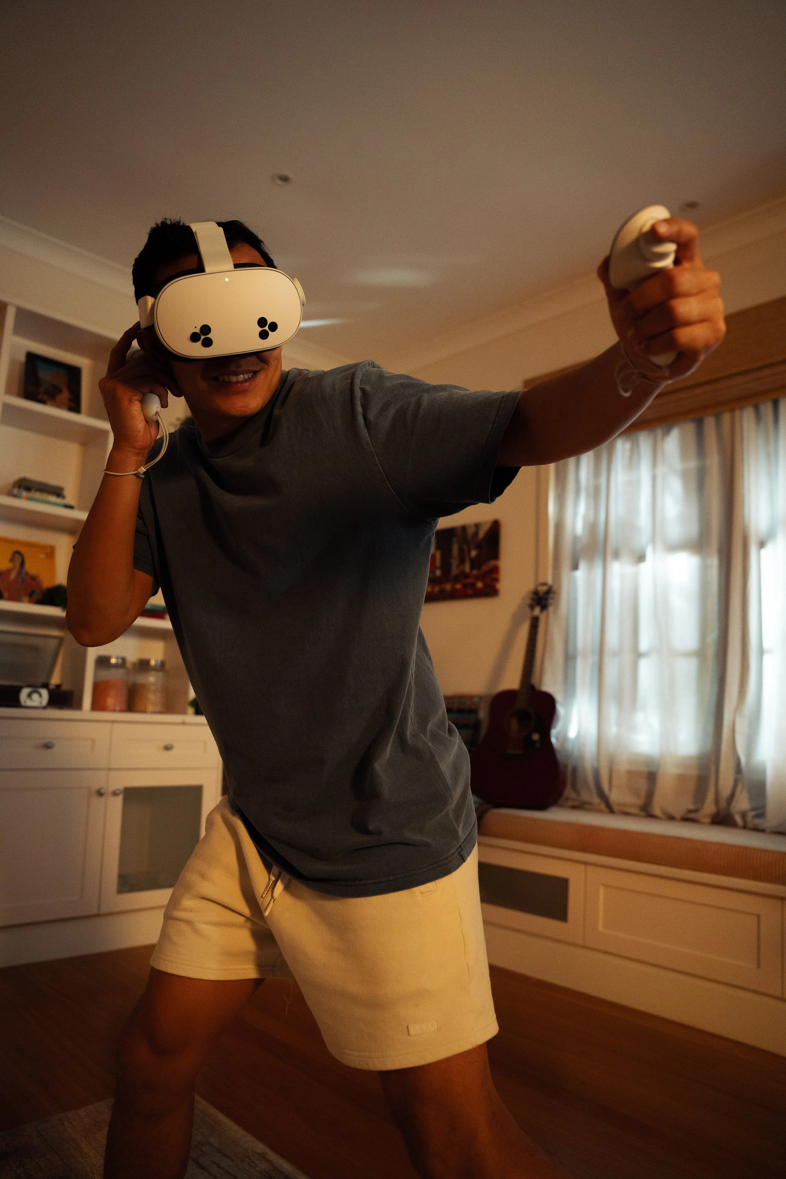 Person wearing virtual reality goggles, holding a controller, and smiling indoors.