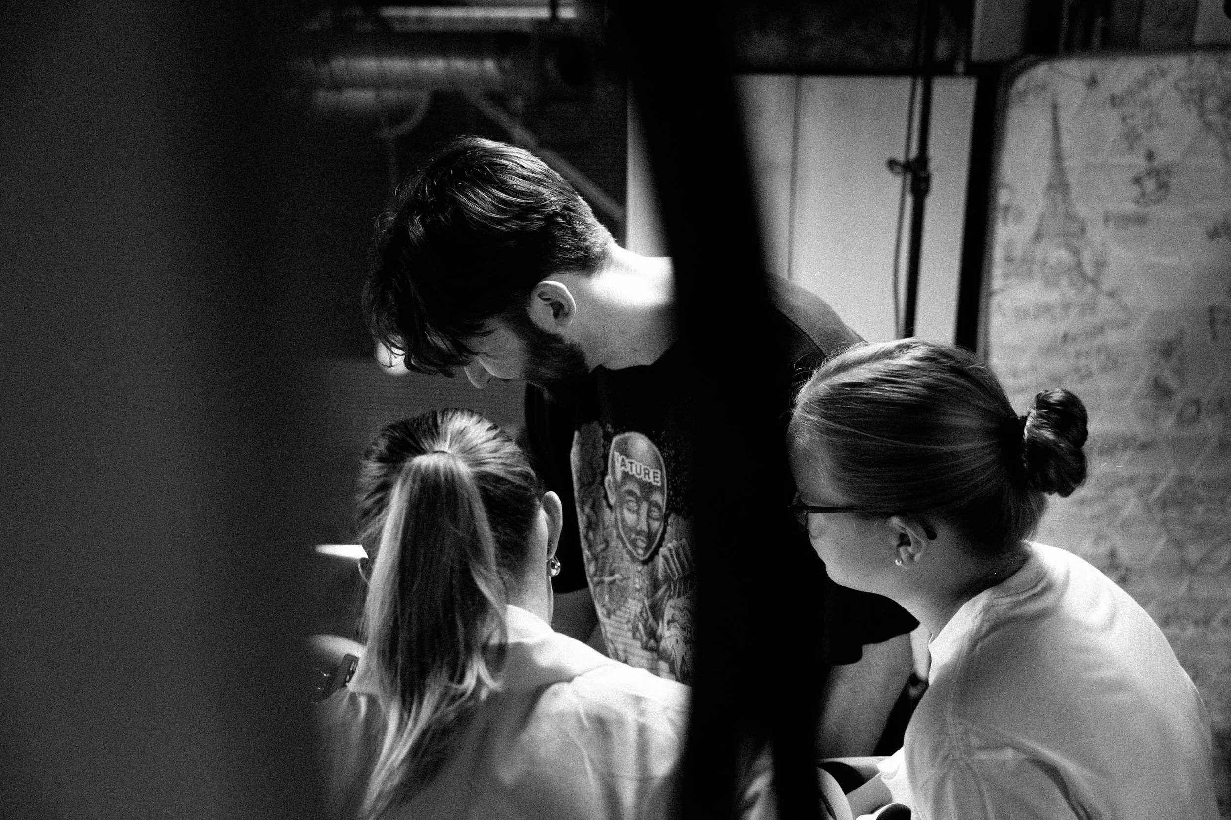 A man with dark hair and a beard leaning over three women sitting down, in a room with a map and whiteboard in the background.