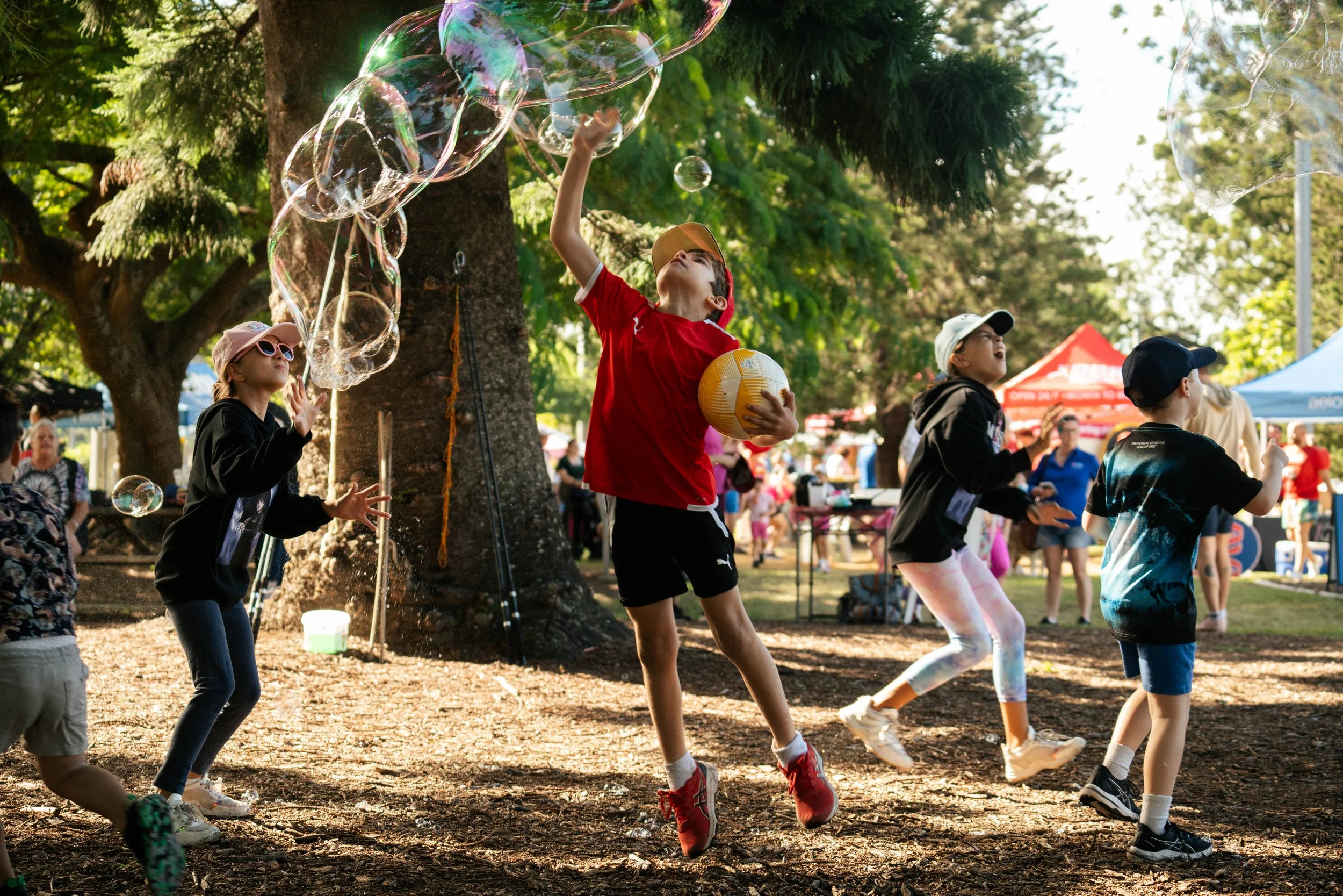 Children playing with bubbles at a park during a community event.