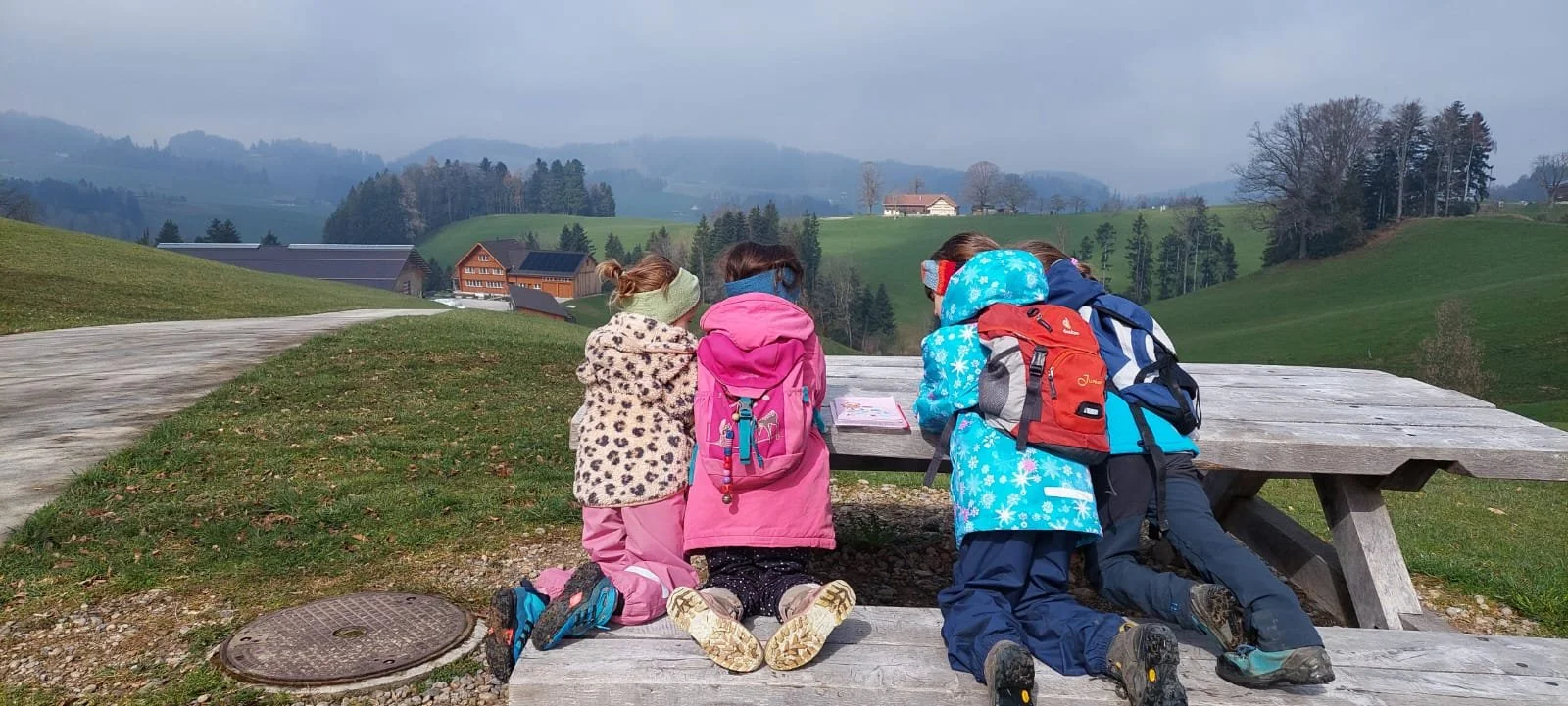 Vier Kinder sitzen an einem Picknicktisch in idyllischer Landschaft und lösen ein spannendes Rätsel