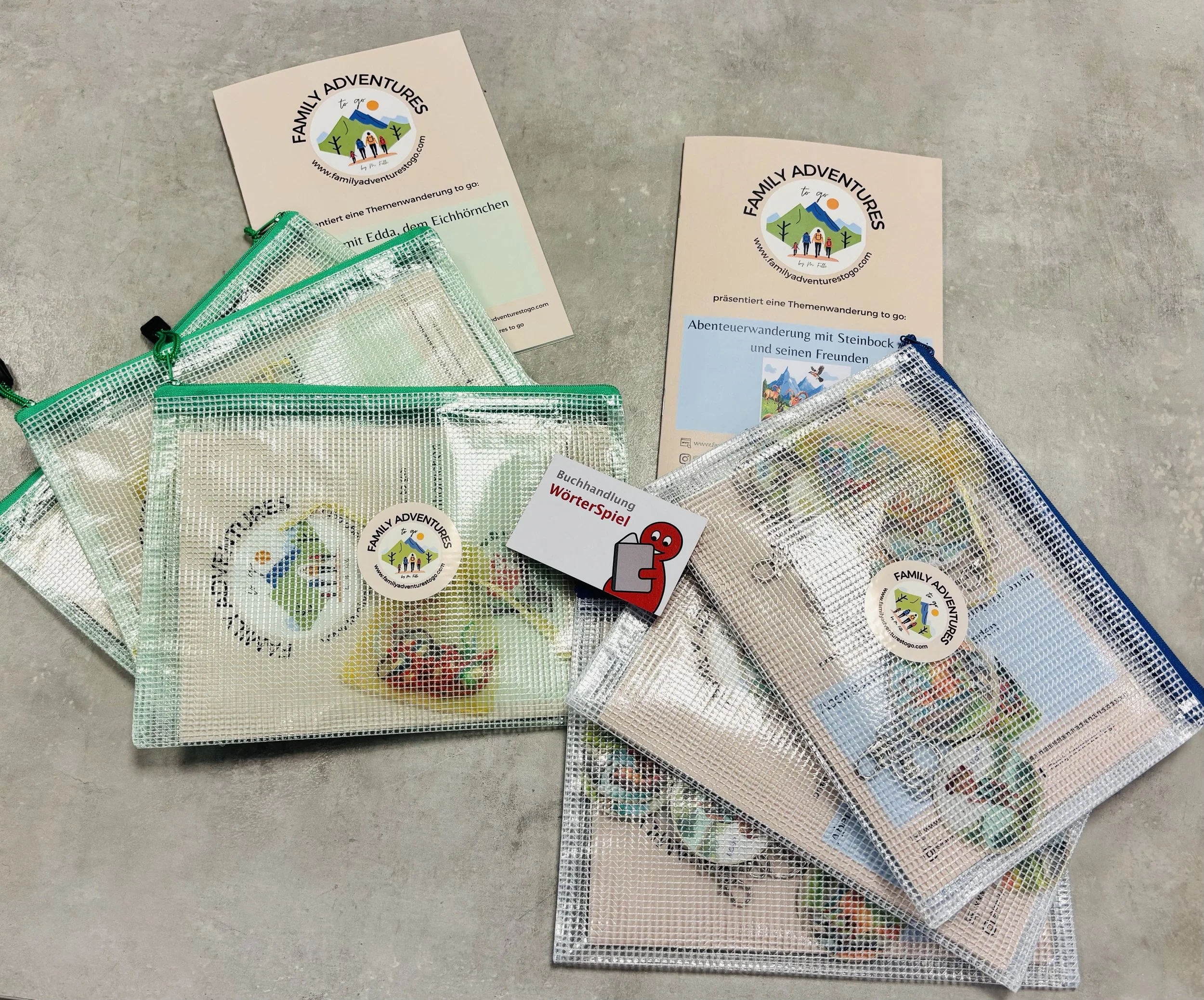 Mehrere kleine Netzbeutel in verschiedenen Farben mit Stickern und Spielmaterialien, zwei Flyer und eine Karte, die zu einer Themenwanderung für Familien einladen.