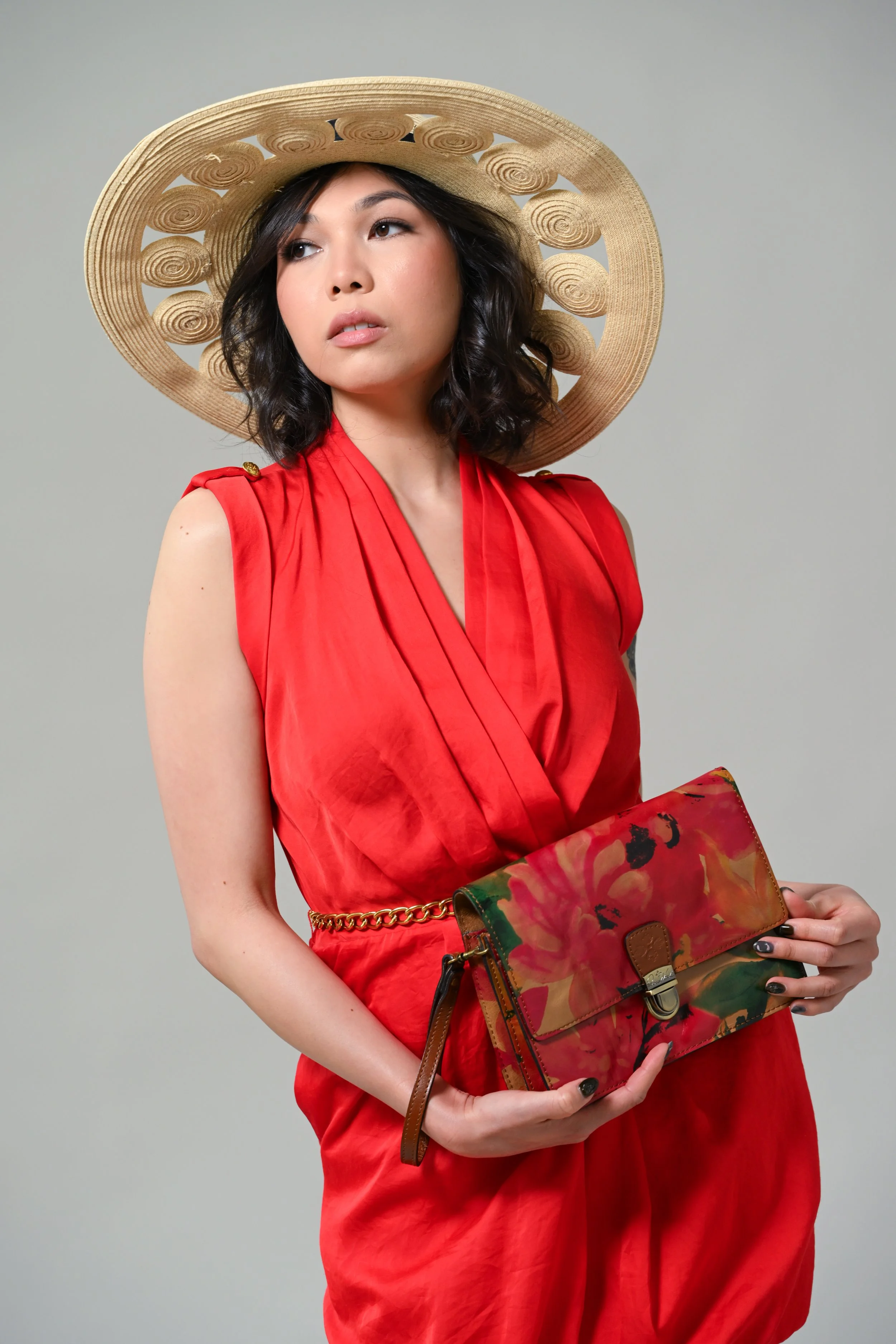 A woman wearing a wide-brimmed straw hat, a red sleeveless dress, and holding a floral-patterned clutch purse.