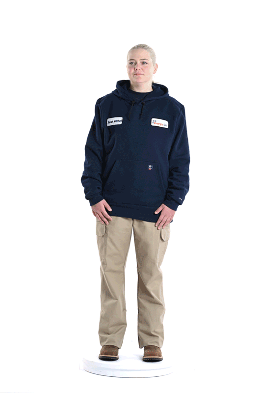 Young woman wearing a navy hoodie with a name tag and sitting in front of a white background.