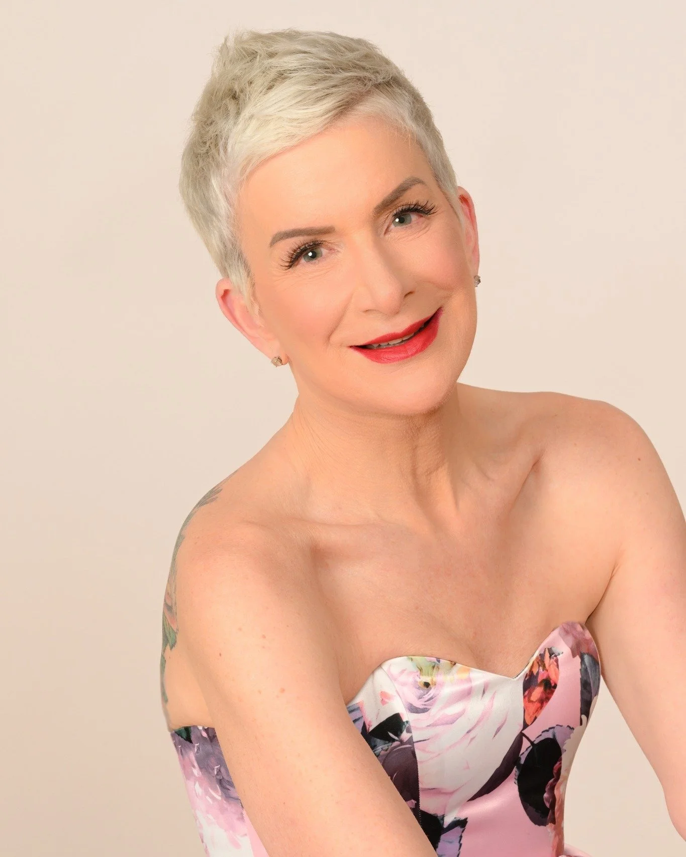 A cream-colored ceramic vase with a narrow neck and wider base holding a dry branch with small round seed pods, placed on a wooden surface with a soft shadow cast on a plain wall.