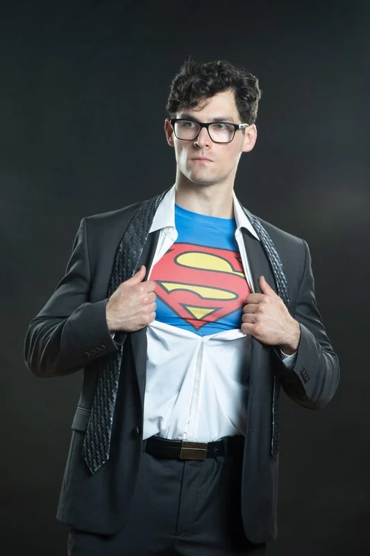 A man in a business suit opening his shirt to reveal a Superman logo T-shirt underneath.