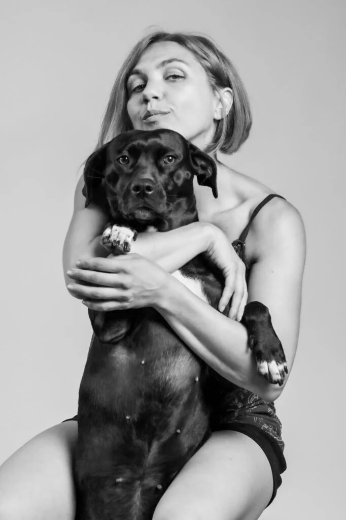Black and white photo of a woman with short hair holding a large dog in her arms, looking at the camera with a neutral expression.