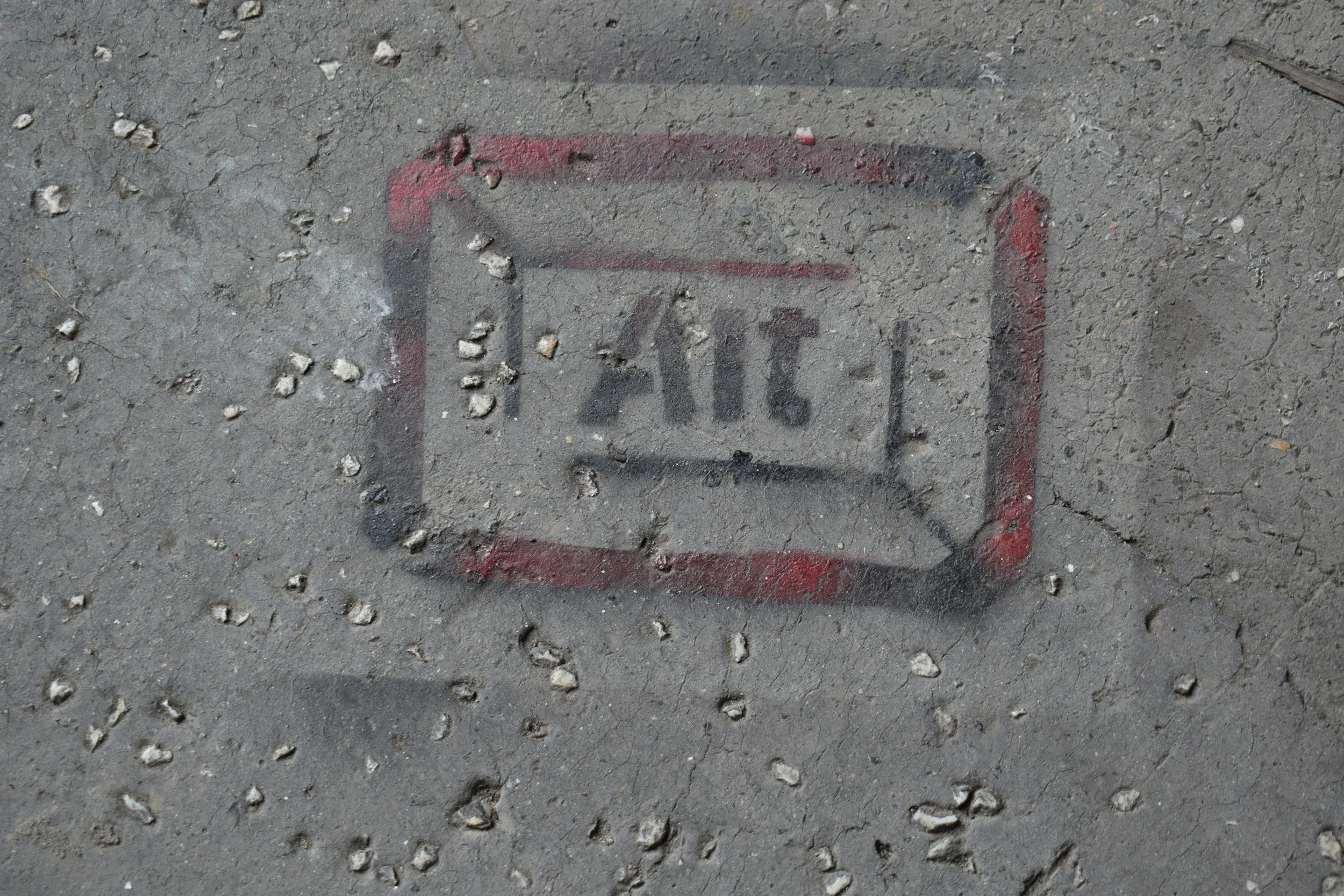 Street art graffiti of a smartphone with the word 'ACT' in the screen area, painted on a cracked concrete sidewalk with small pebbles surrounding it.