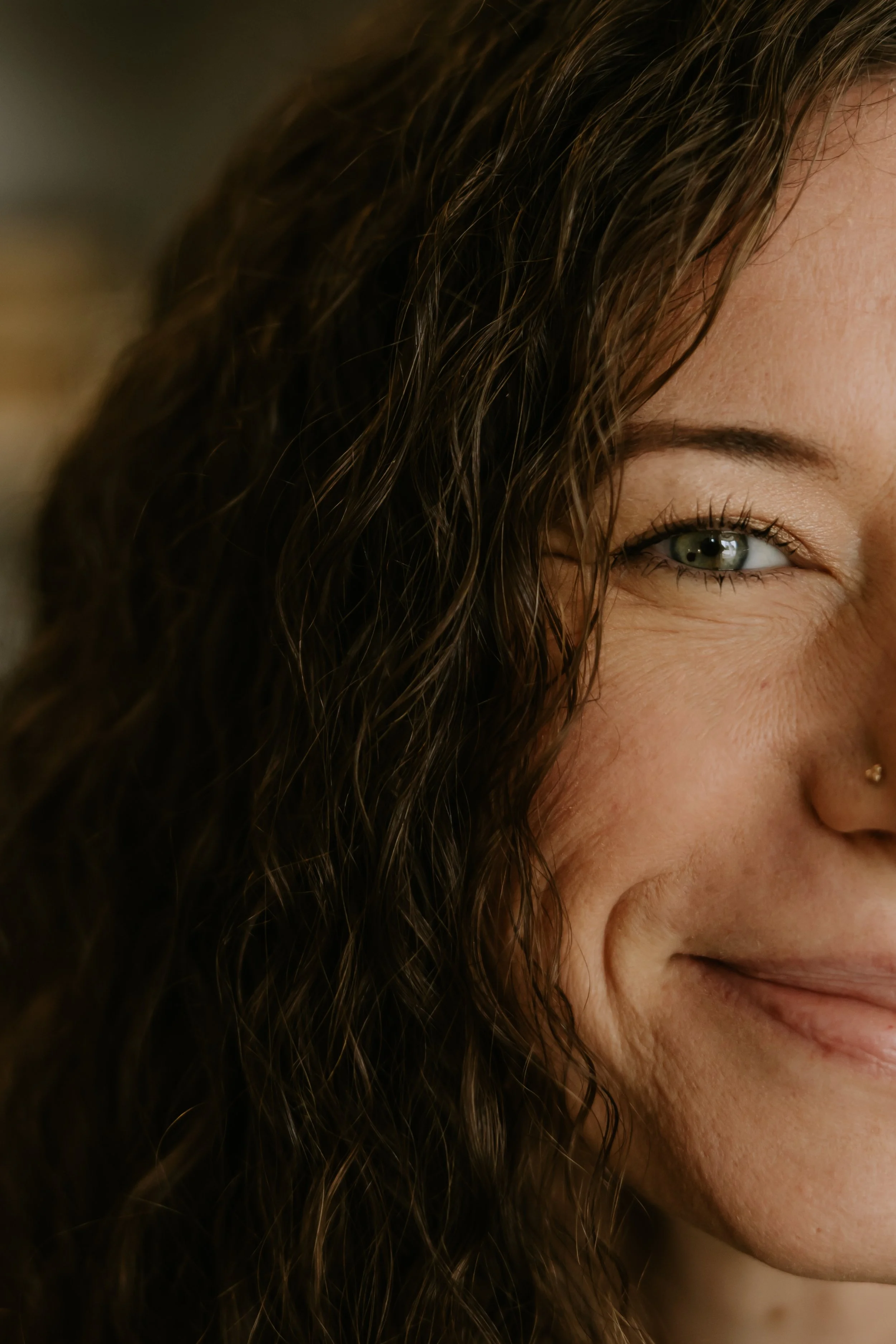 Close-up of a smiling woman's face, showing her eye, cheek, and part of her lips, with curly brown hair.