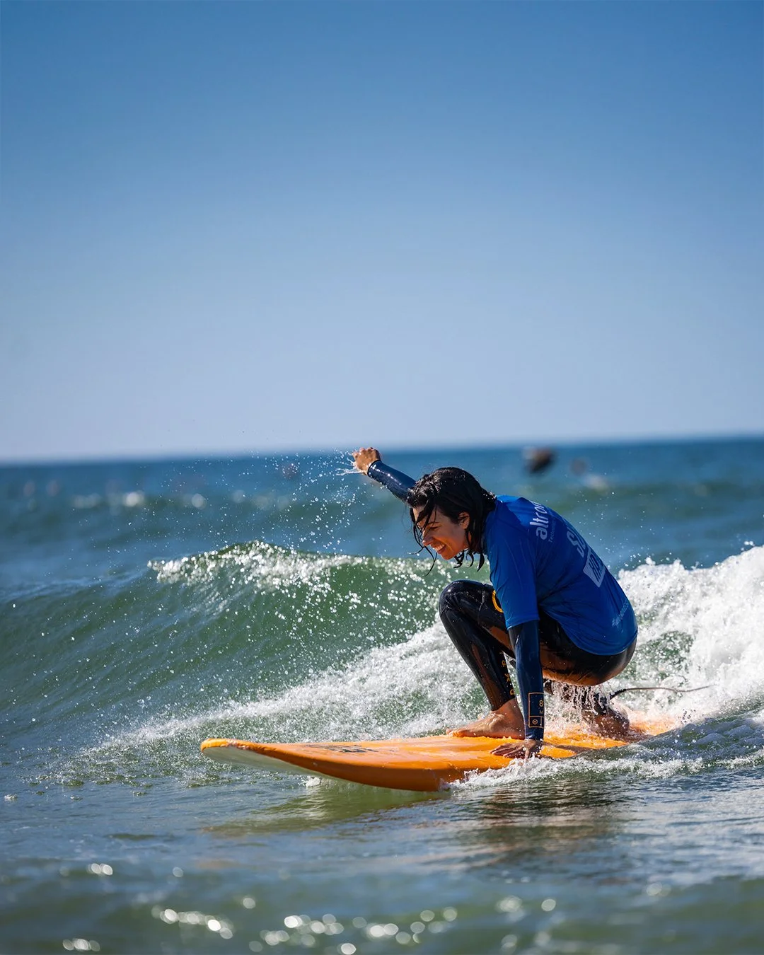 A woman surfing on a wave in the ocean, wearing a blue wetsuit and smiling.