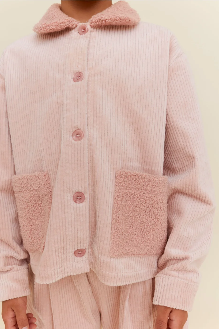 A person wearing a pink corduroy jacket with fuzzy pink collar and pocket accents.