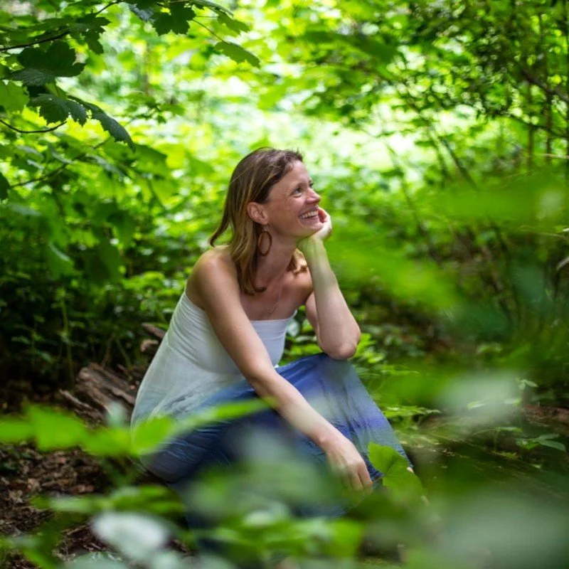 Artist Anna Neubert-Wood also known as WanderWomen photographed crouched and smiling amongst woodland scenery