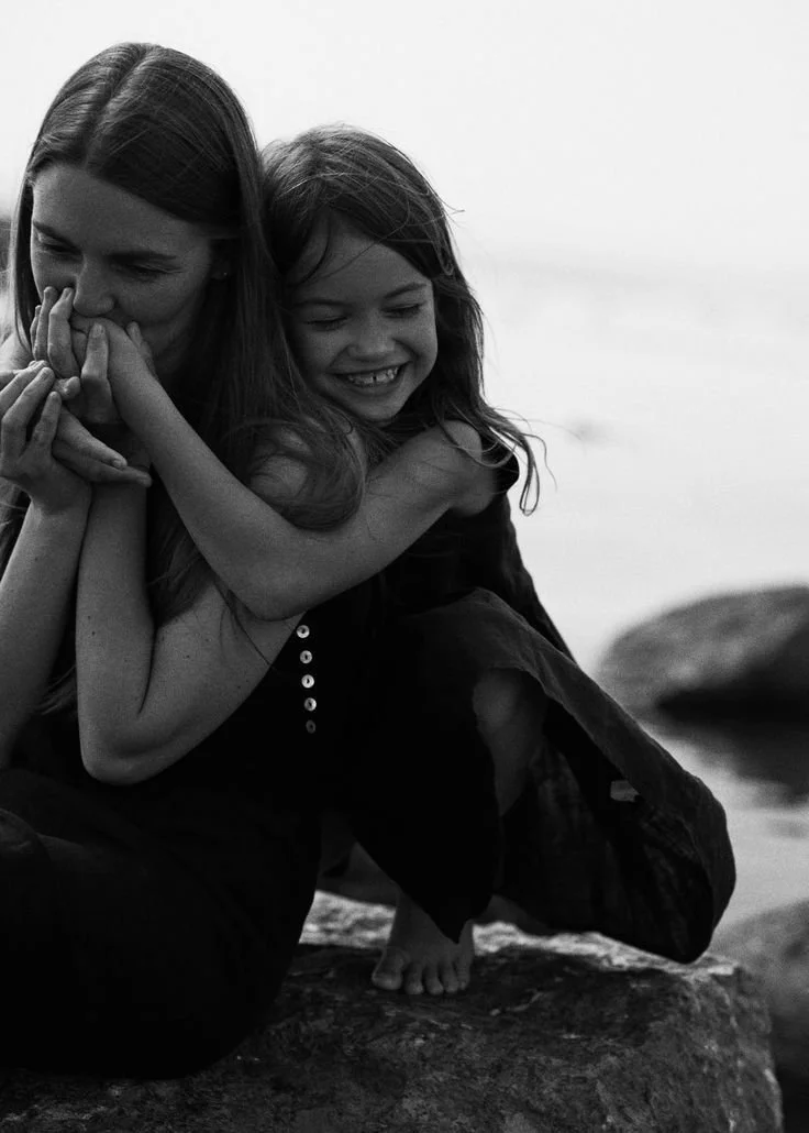 Zwei lachende Mädchen, die sich umarmen und auf einem Felsen sitzen, im Schwarz-Weiß-Foto an der Küste