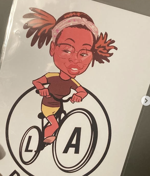 Cartoon drawing of a girl with glasses and a headband riding a bicycle with the letters 'L' and 'A' on the wheels.