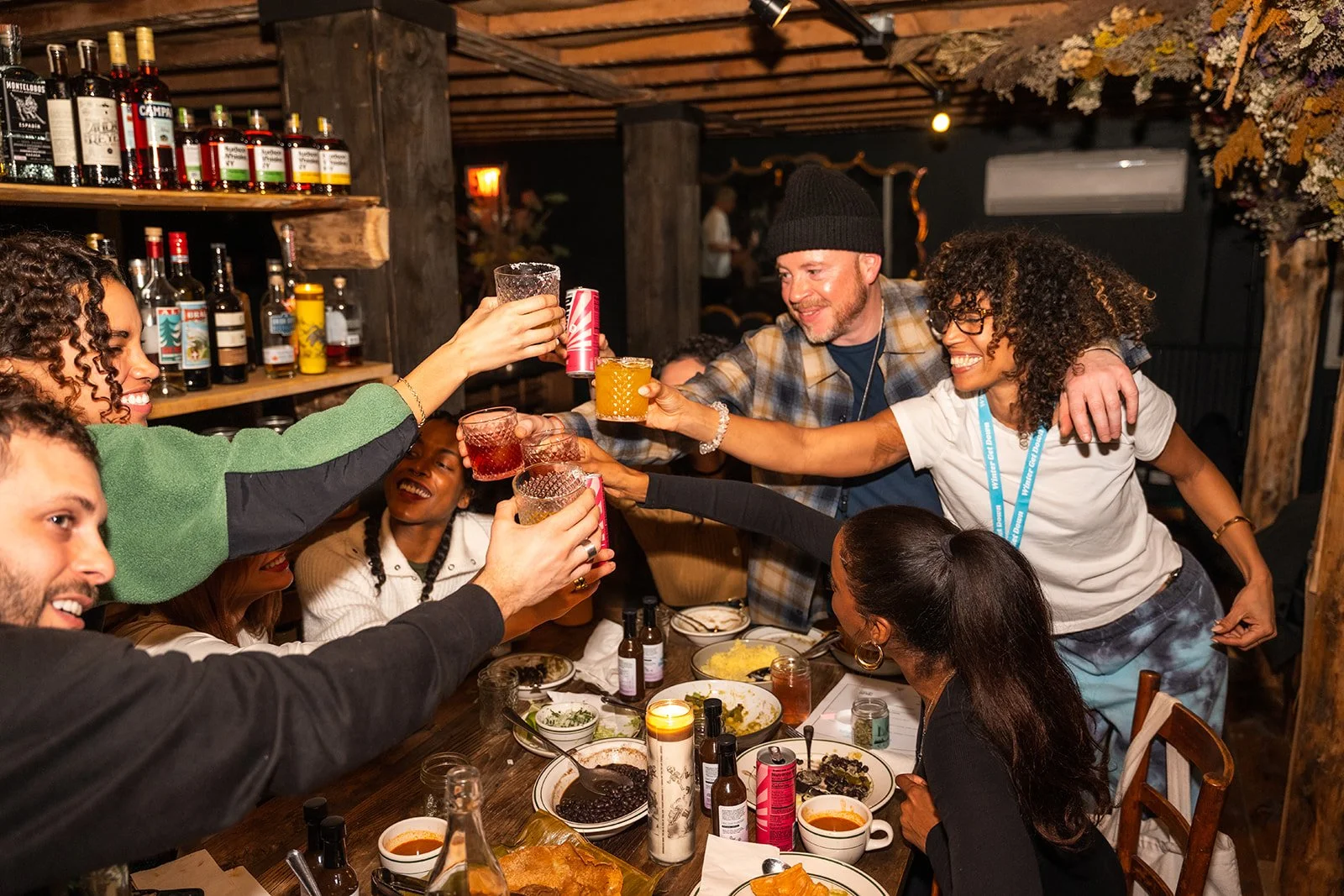 People gathered around a dinner table celebrating with drinks, raising glasses in a toast, in a cozy restaurant setting.
