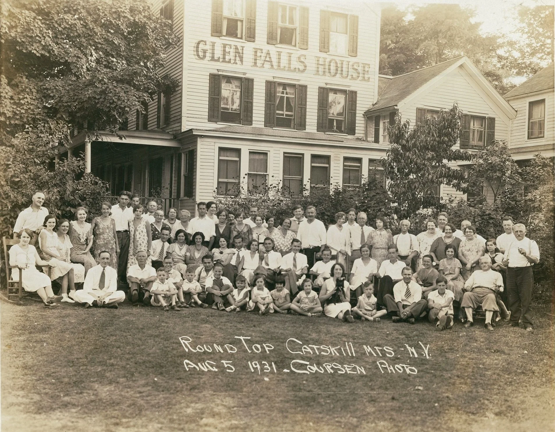 A large group of men, women, and children posed in front of a house labeled 'Glen Falls House,' with trees and garden area around them, taken during a gathering on August 5, 1931.