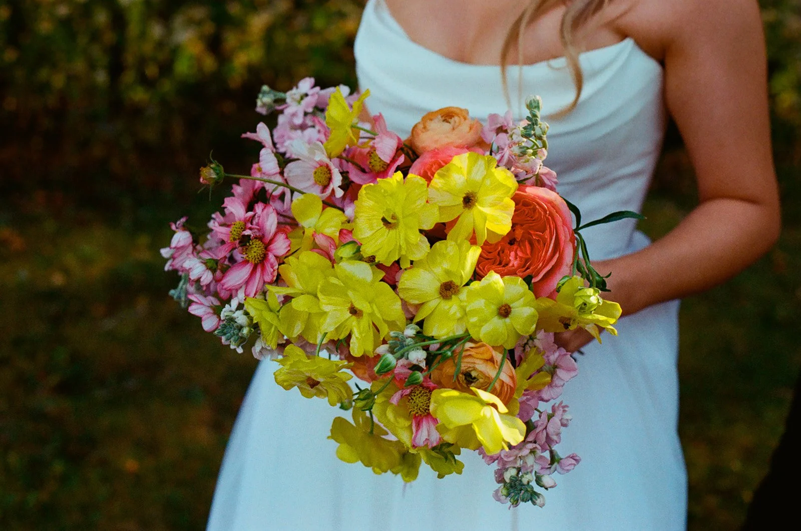 A woman in a white dress holding a colorful bouquet of pink, yellow, and orange flowers.