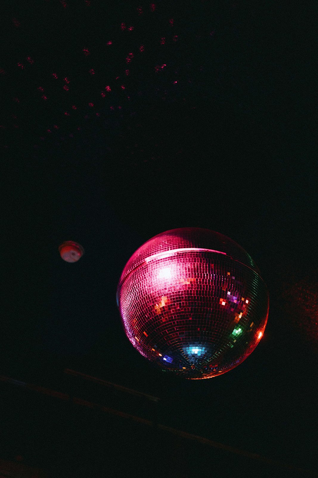 A large disco ball reflecting colorful lights in a dark setting, with smaller lights or reflections above.
