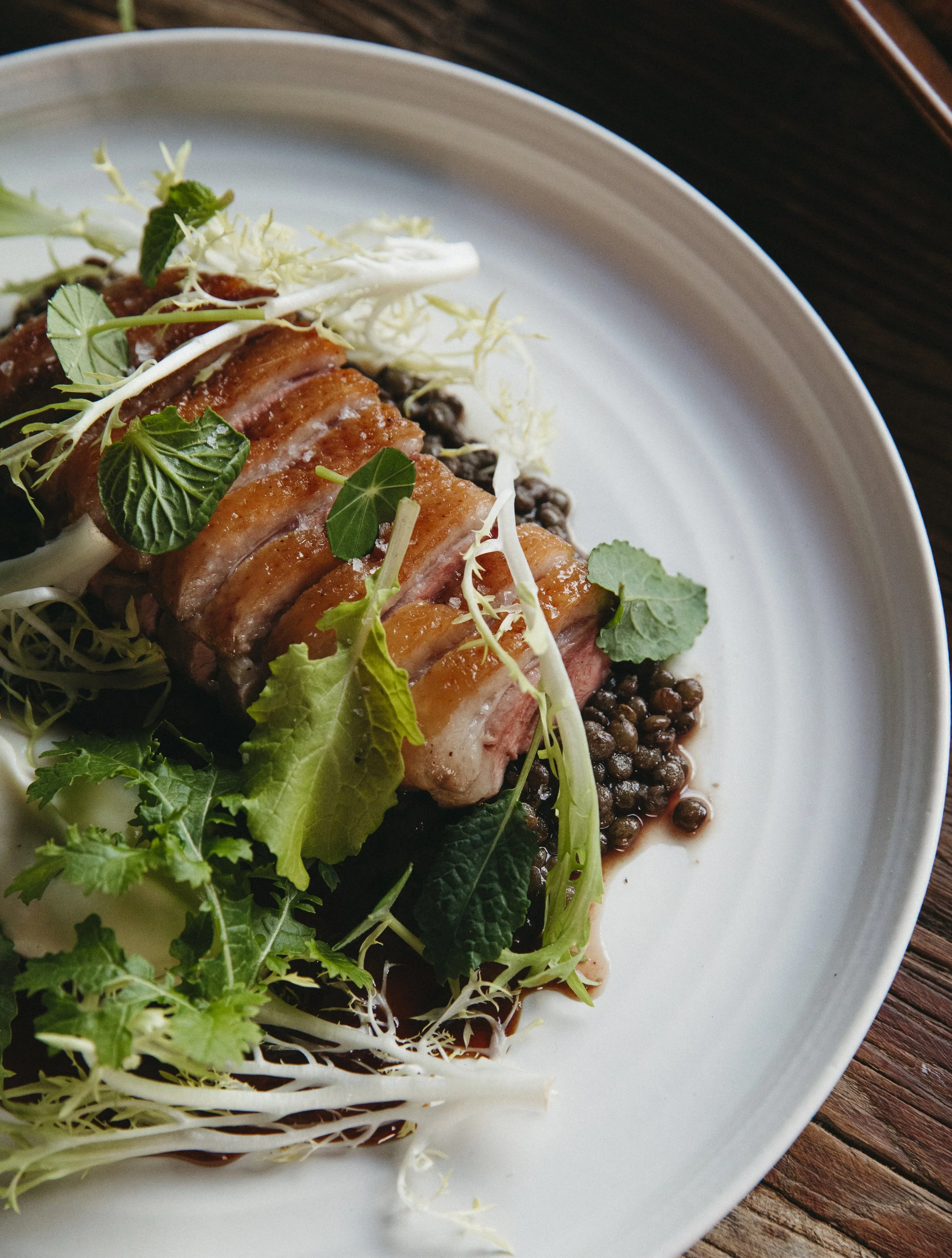 Sliced duck breast on a white plate with mixed greens and lentils