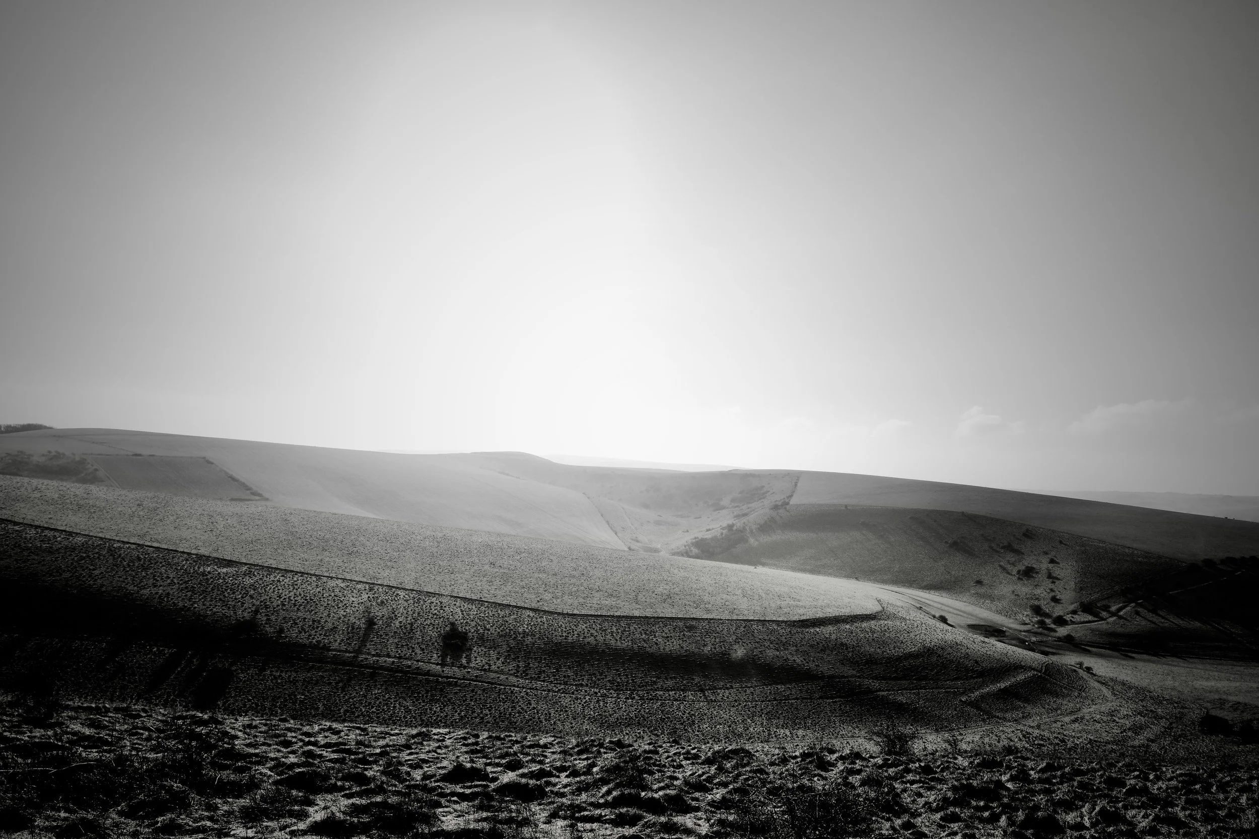 A high contrast black and white photograph of the sun rising onto the South Downs at Mount Caburn near Lewes by John Worth, Artist