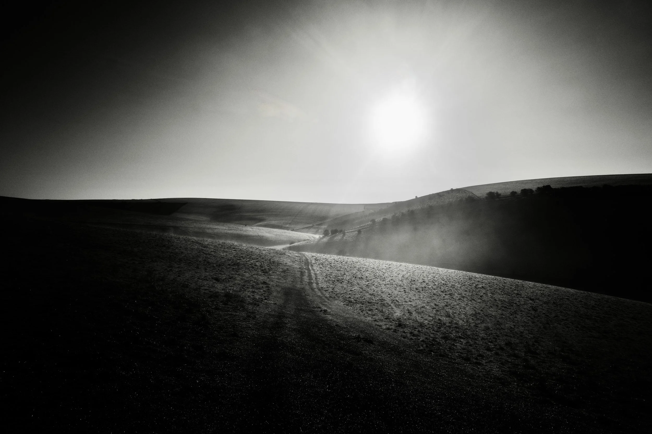 A high contrast black and white photograph of the sun rising onto the South Downs at Mount Caburn near Lewes by John Worth, Artist