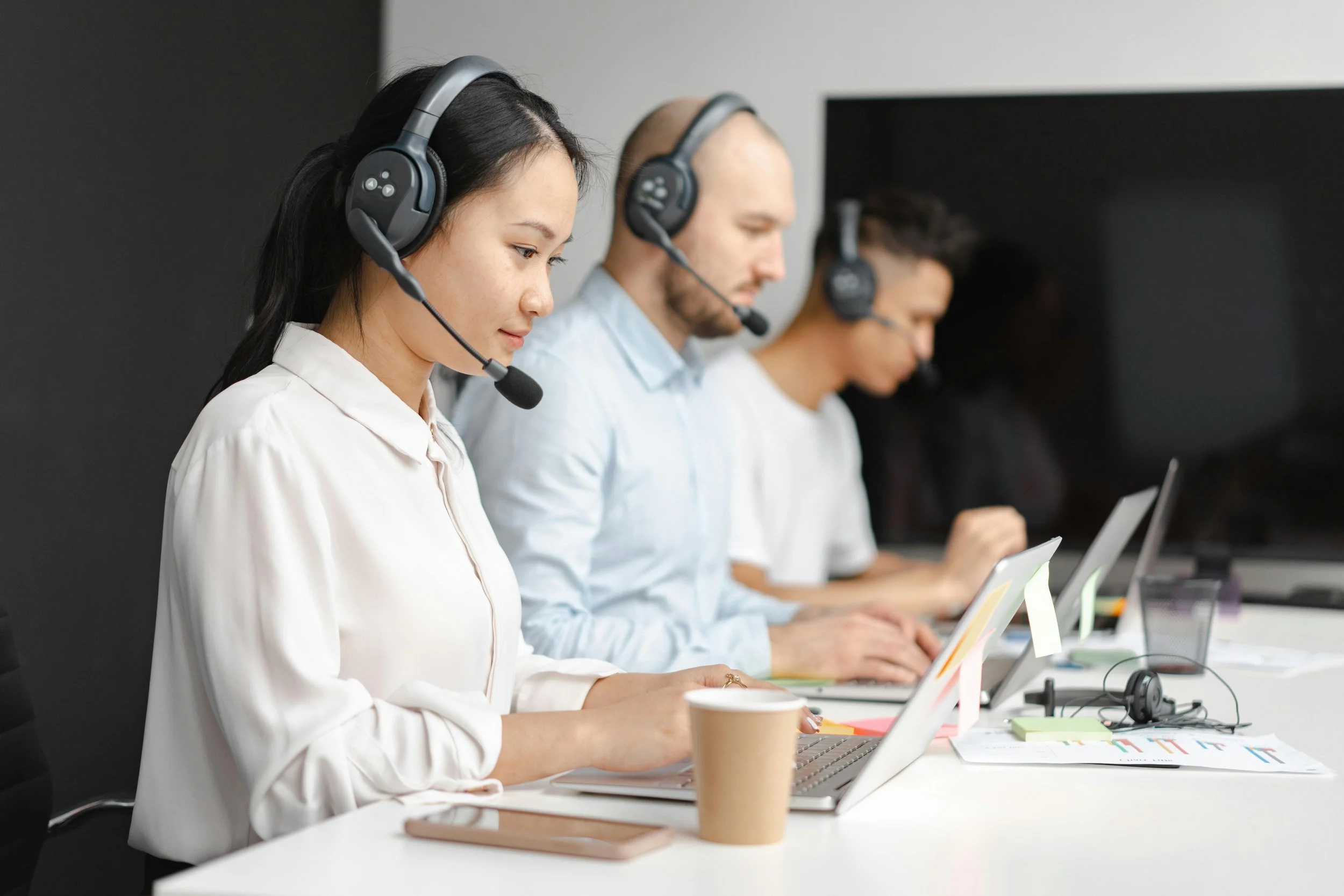 A group of four people wearing headsets working on laptops in a conference room. Sales Development Representatives booking discovery calls for a Saas company
