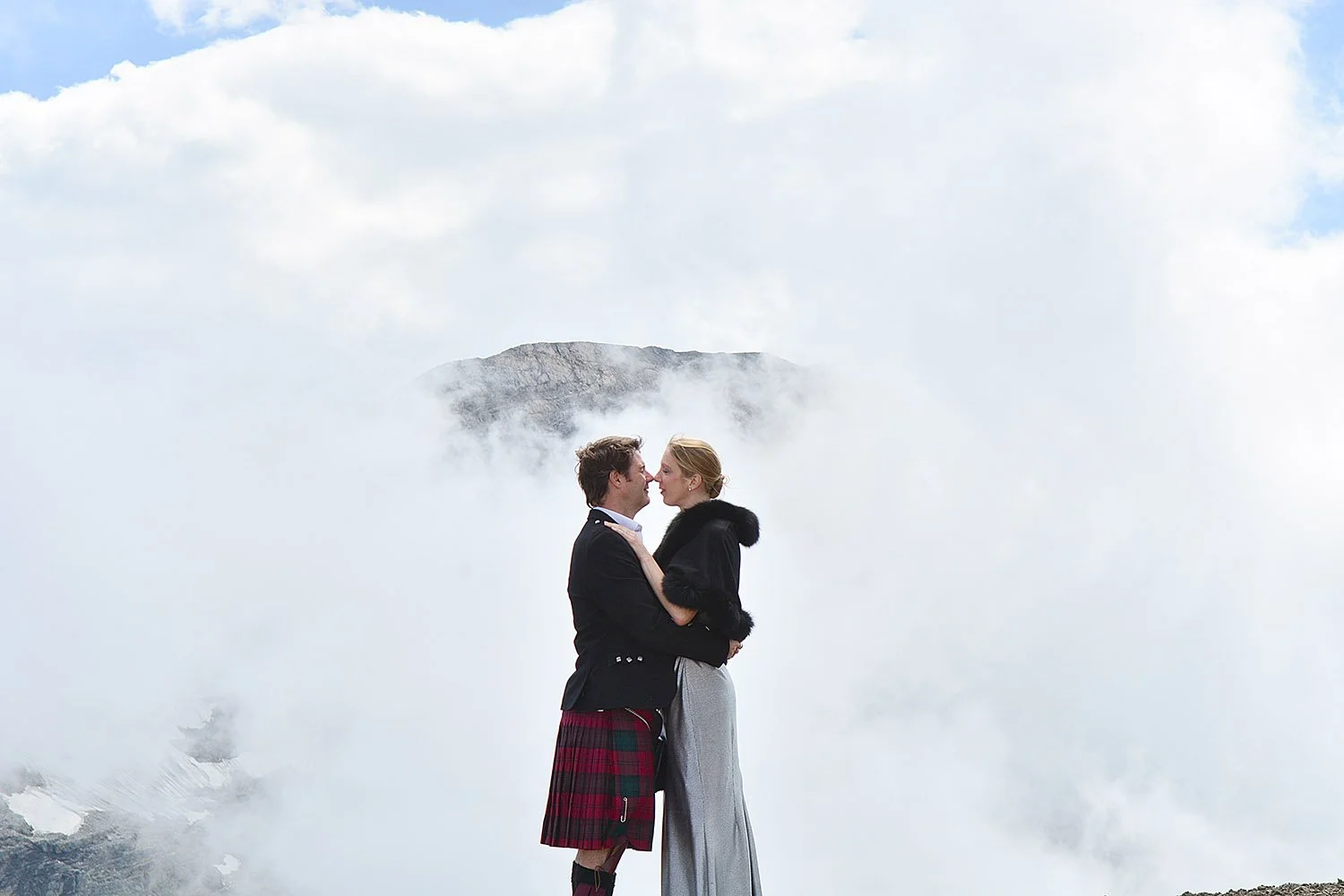 Un couple qui se tient dans un paysage brumeux, avec une montagne en arrière-plan, se regardant tendrement.