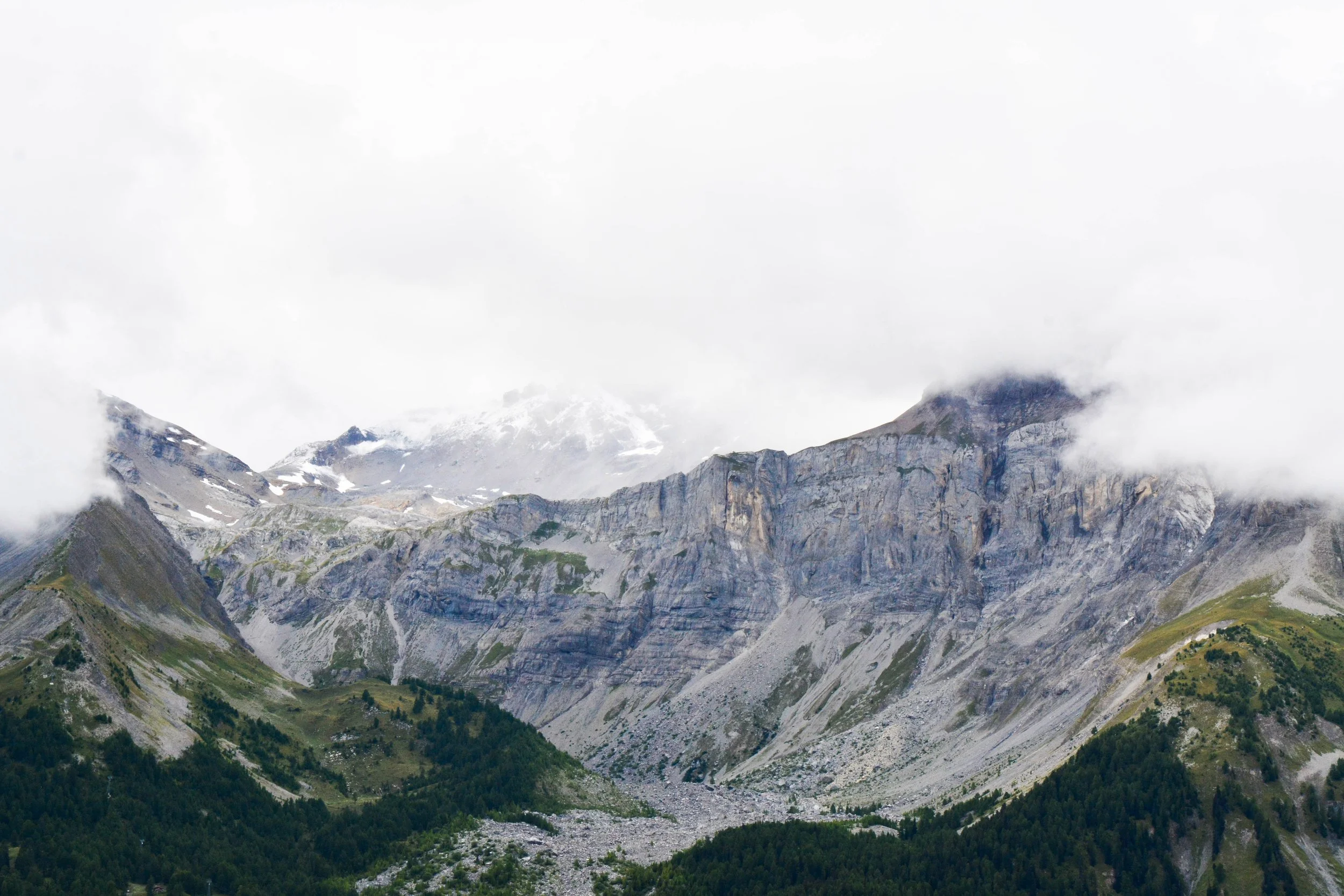 Montagnes Rocheuses avec sommets enneigés et forêt au premier plan sous un ciel nuageux.