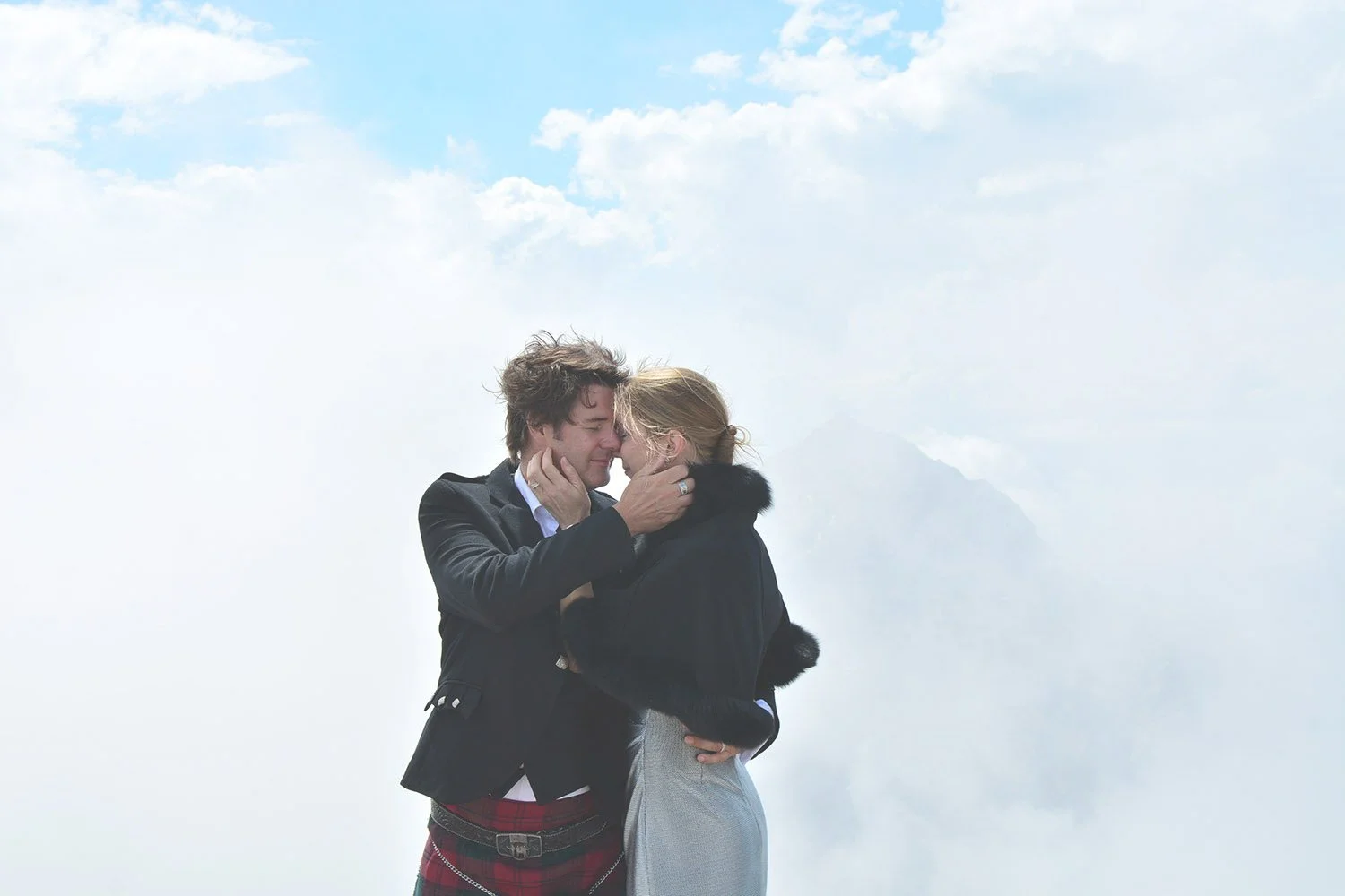 Un couple s'enlace tendrement sous un ciel nuageux en montagne.