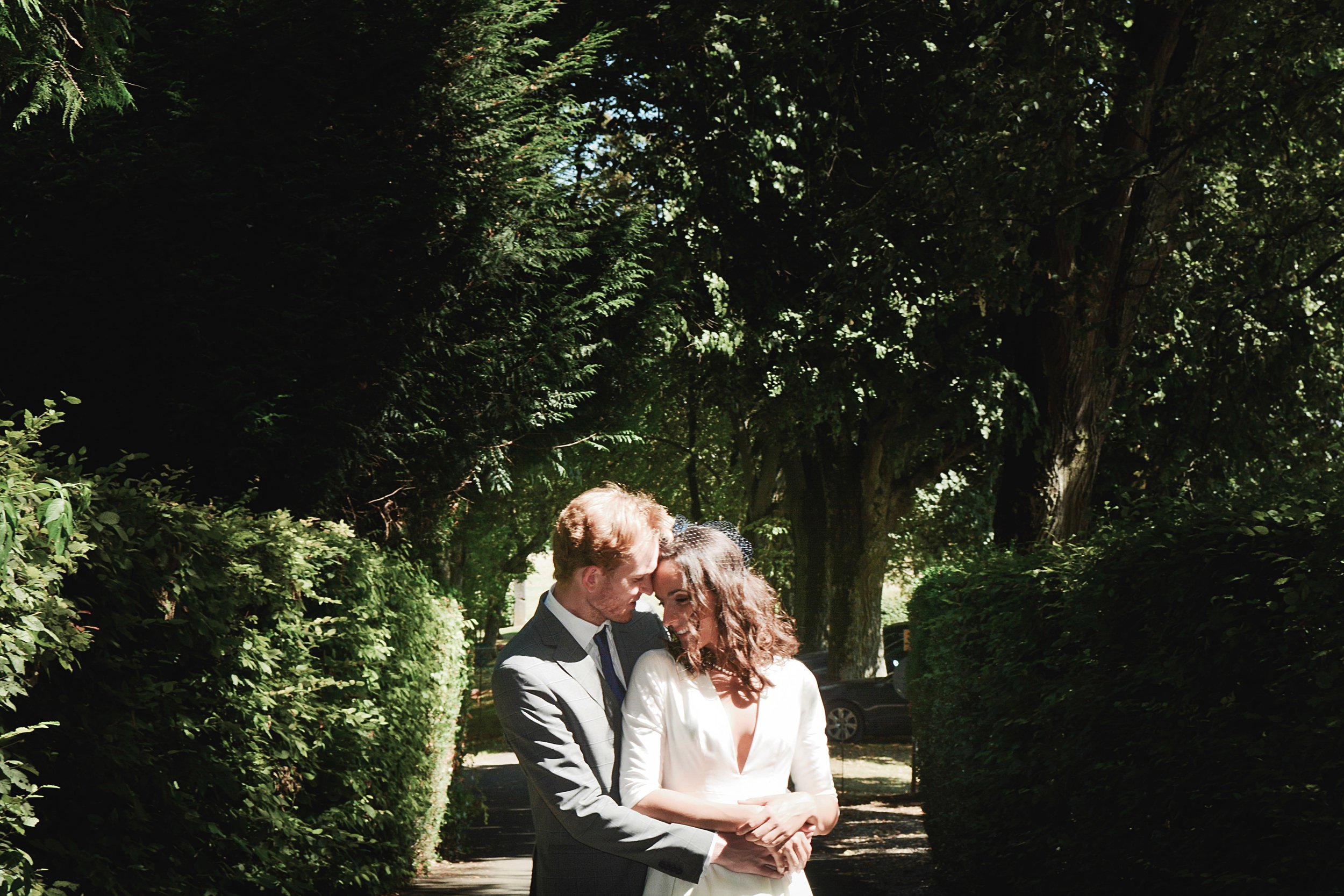 Un couple en costume de mariage devant un arbre dans un parc, se regardant tendrement.