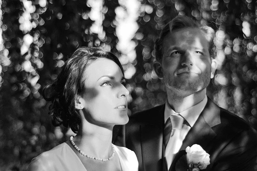 Un homme et une femme en costume élégant, possiblement lors d'un mariage, dans un décor extérieur avec des arbres en arrière-plan, photographiés en noir et blanc.