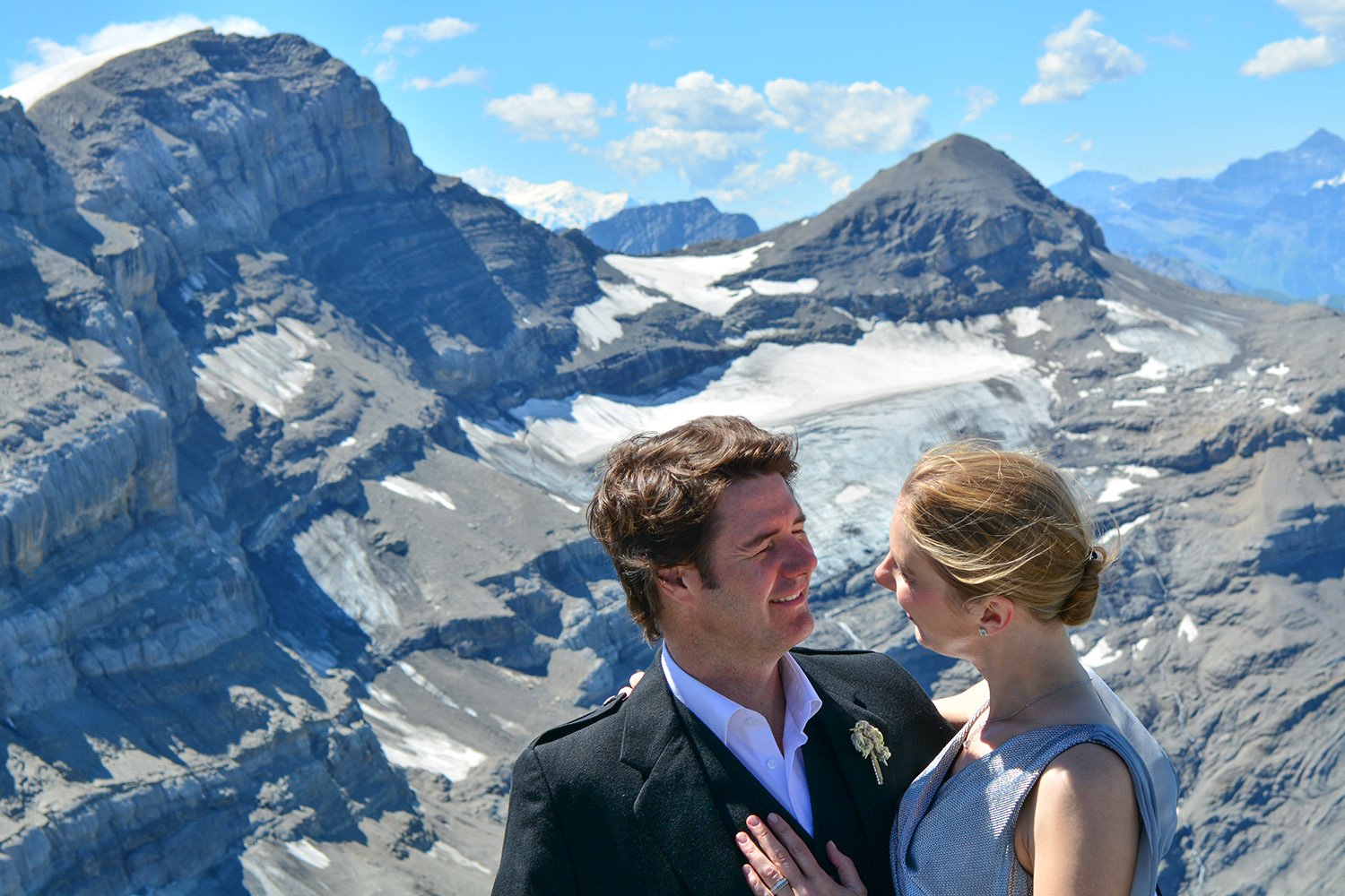 Un couple de mariés s'embrasse dans un paysage de montagnes enneigées avec un petit glacier.