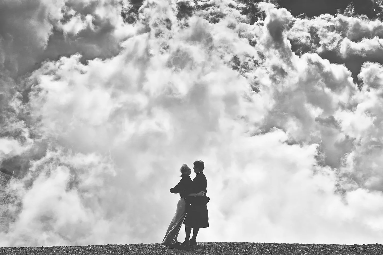 Silhouettes d'un homme et d'une femme se tenant par la taille, se regardant tendrement, sur un arrière-plan de ciel nuageux.