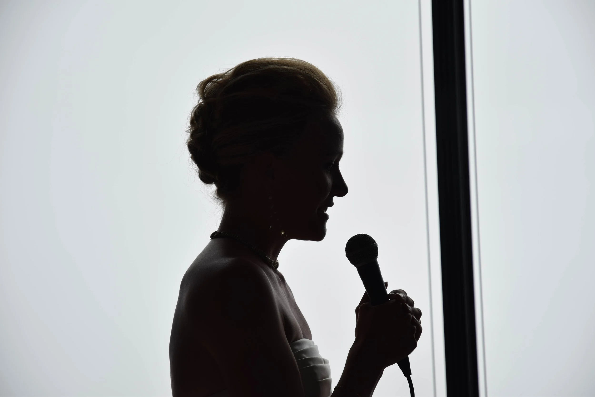 silhouette d'une femme parlant dans un microphone avec un arrière-plan lumineux