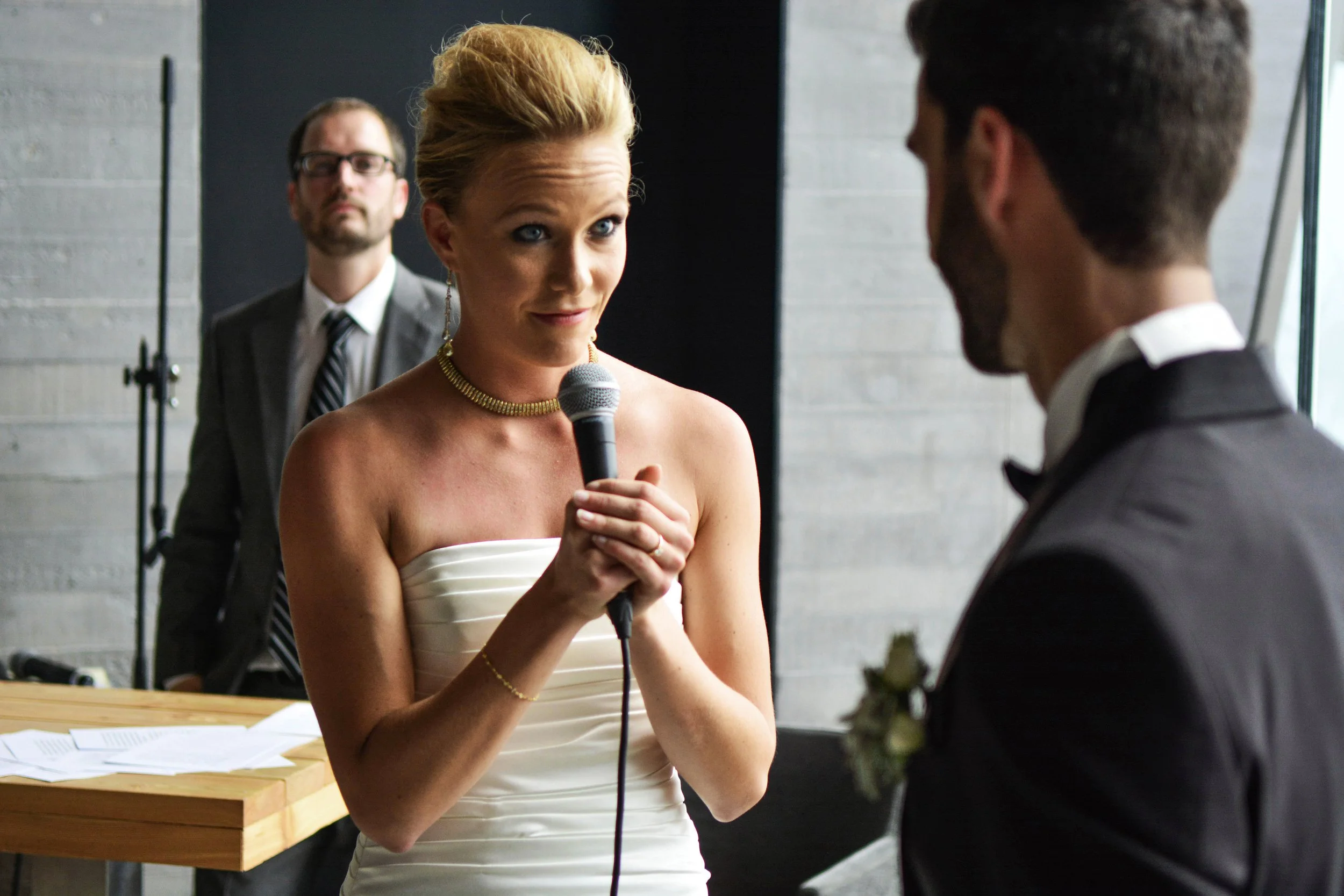 Femme en robe blanche parlant dans un microphone lors d'une cérémonie de mariage, homme en costume noir à côté, arrière-plan avec homme en costume pour la sonorisation.