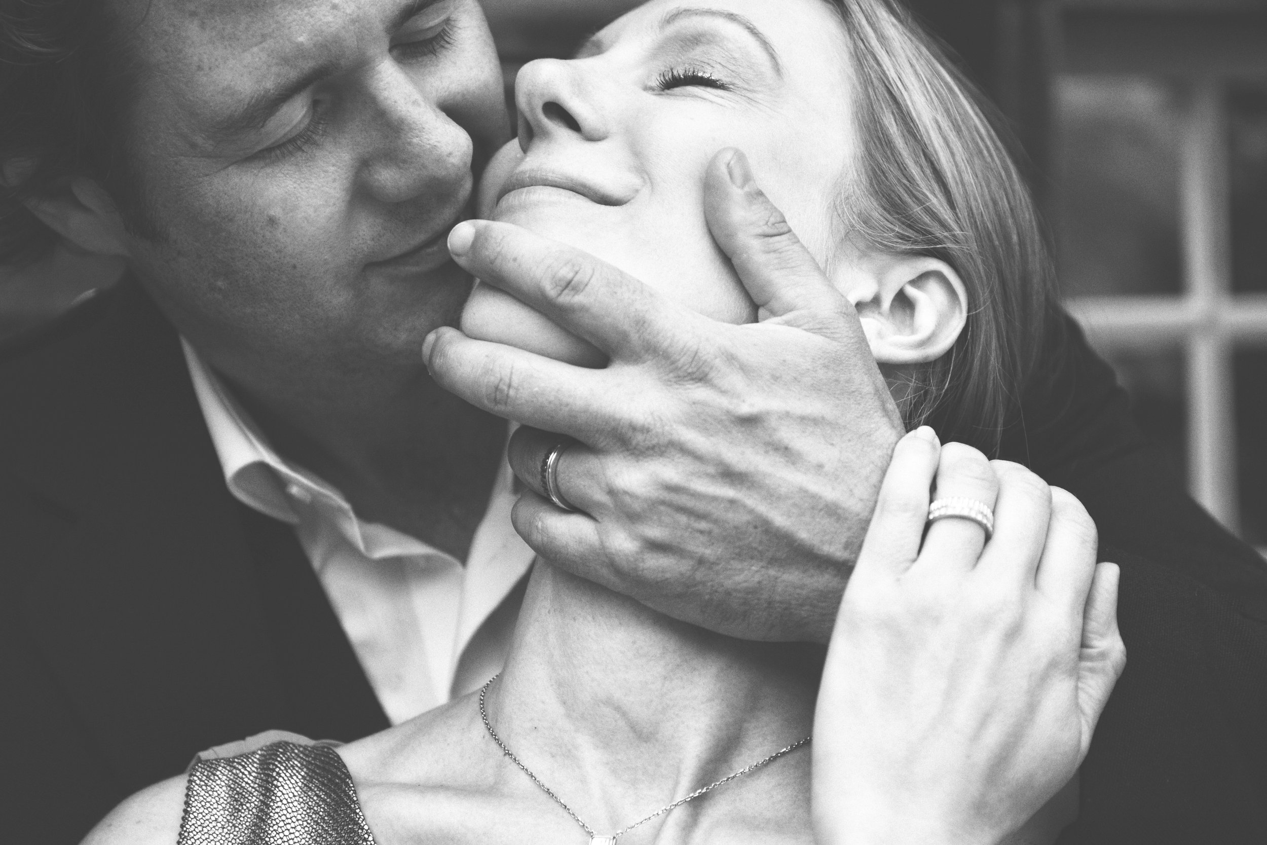 Un couple s'embrasse de près, l'homme tenant le visage de la femme et ils portent des alliances.