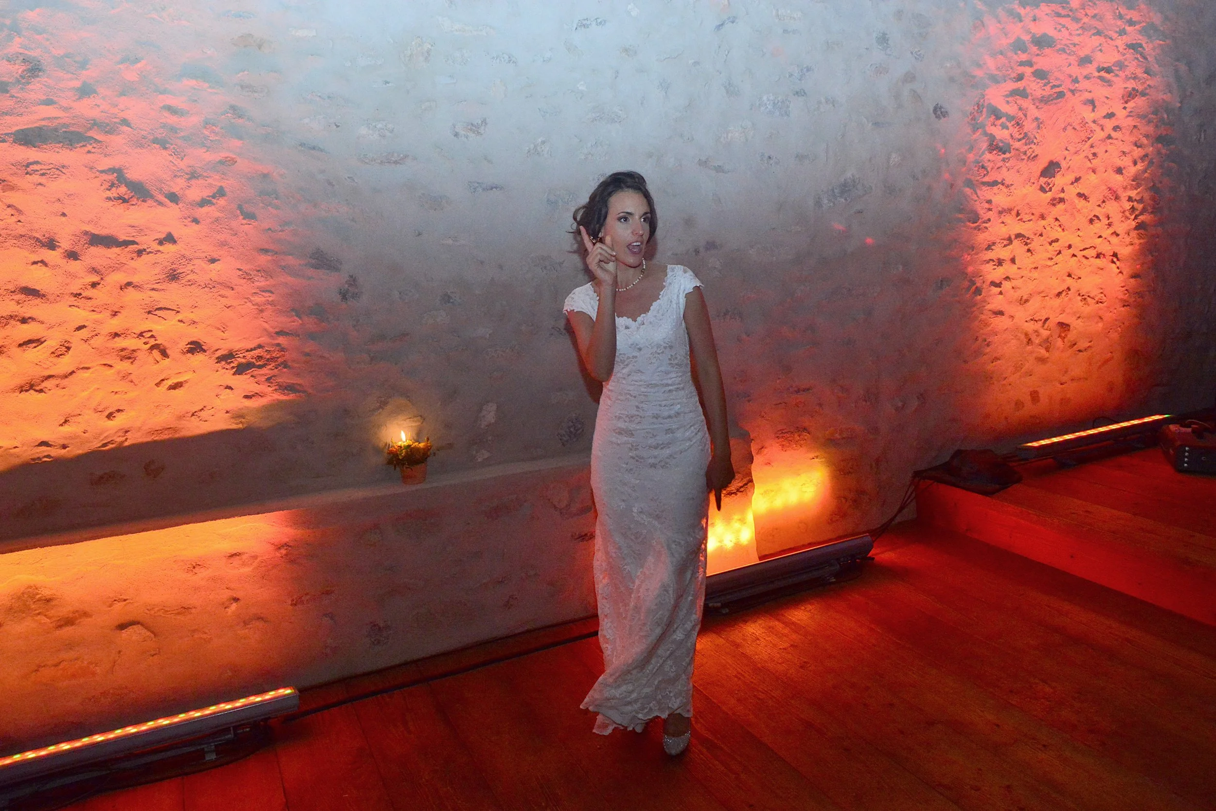Femme en robe blanche en train de danser dans une pièce avec un mur en pierre et un éclairage orange.
