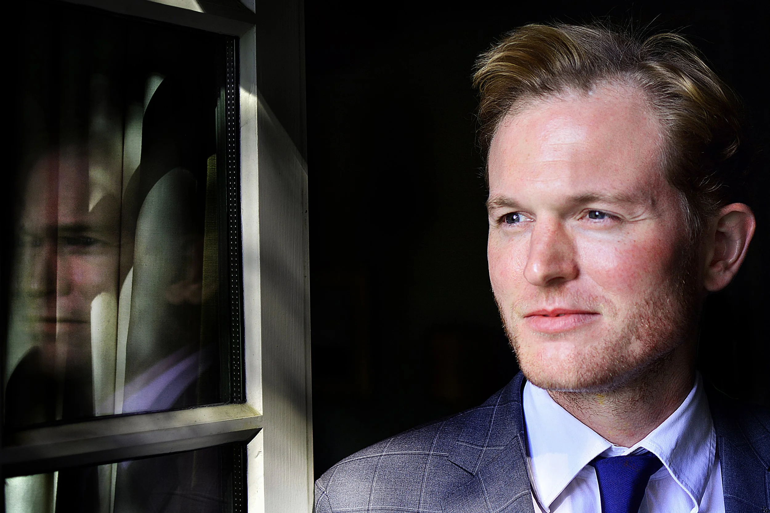 Jeune homme en costume regardant pensivement par une fenêtre