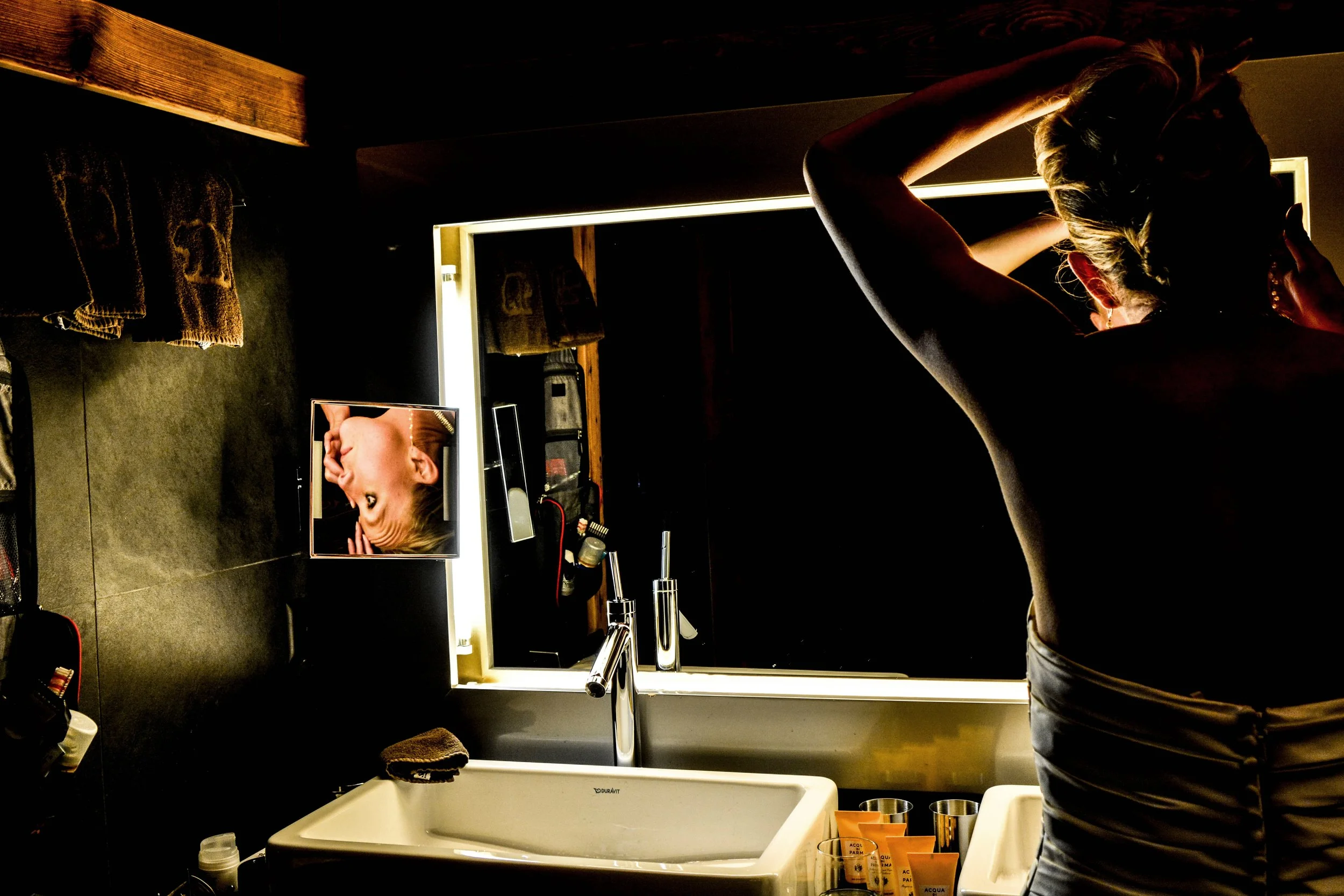 Femme se préparant dans une salle de bain, ajustant ses cheveux devant un miroir éclairé.