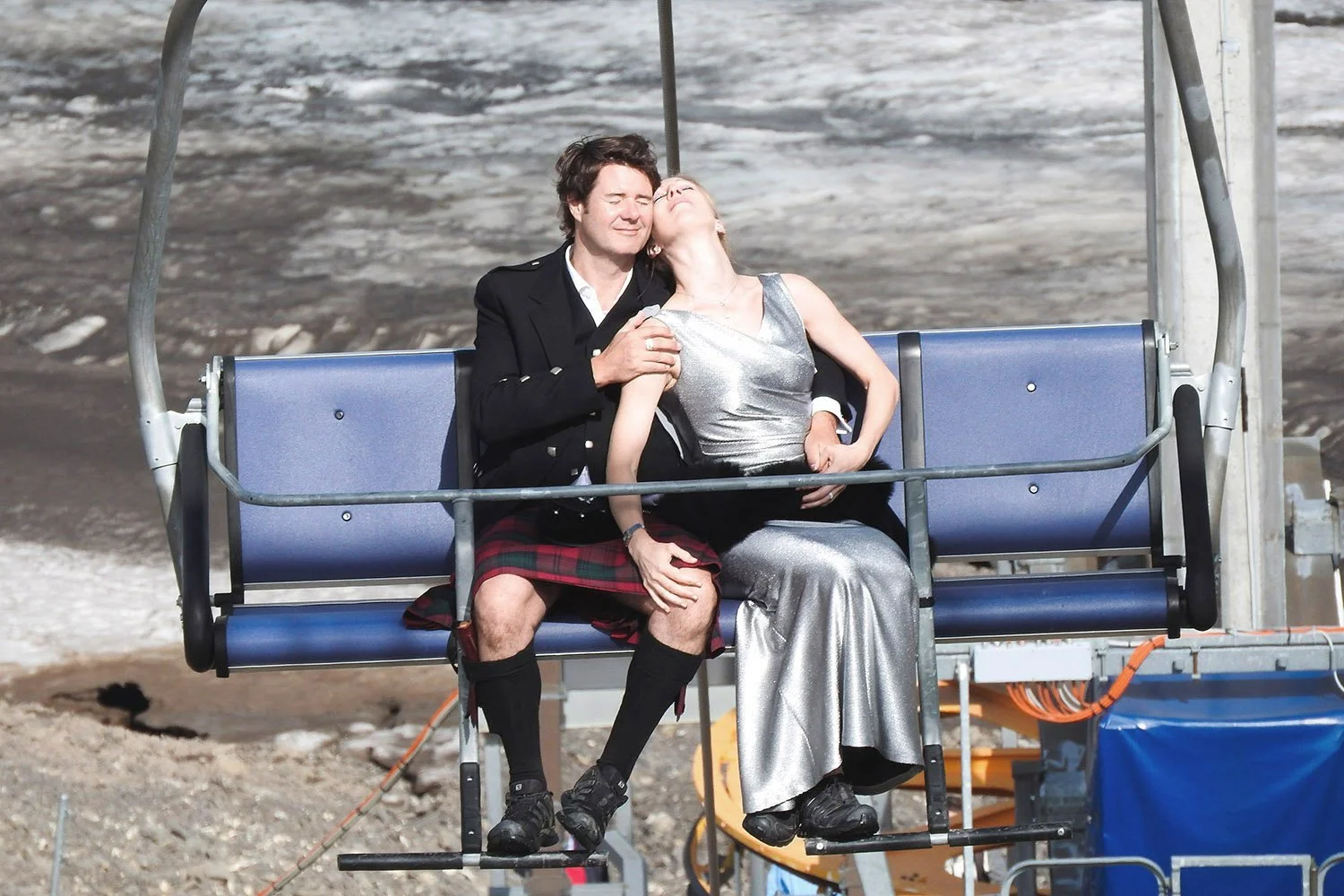 Deux personnes assises sur une chaise de télésiège dans un paysage rocheux, semblant profiter d'un moment de bonheur ensemble.