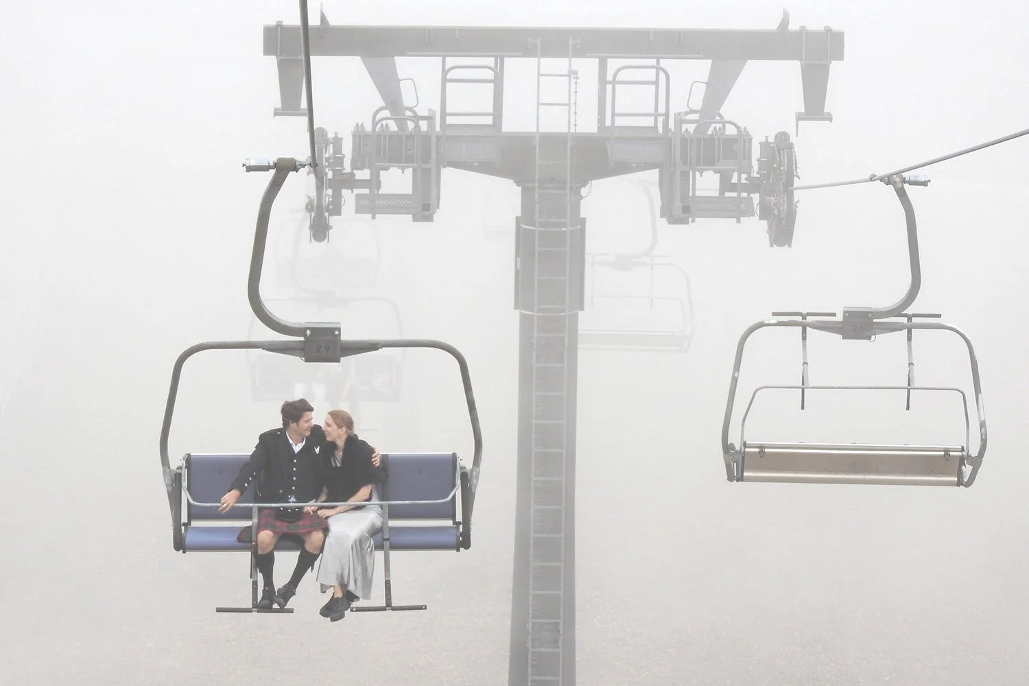 Deux personnes assises sur une chaise en cabine de téléphérique, enveloppées de brouillard.