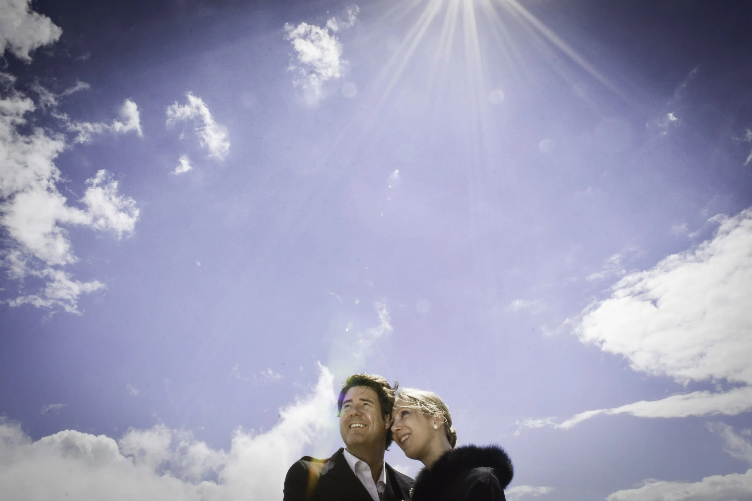Un couple souriant sous un ciel bleu ensoleillé avec quelques nuages.